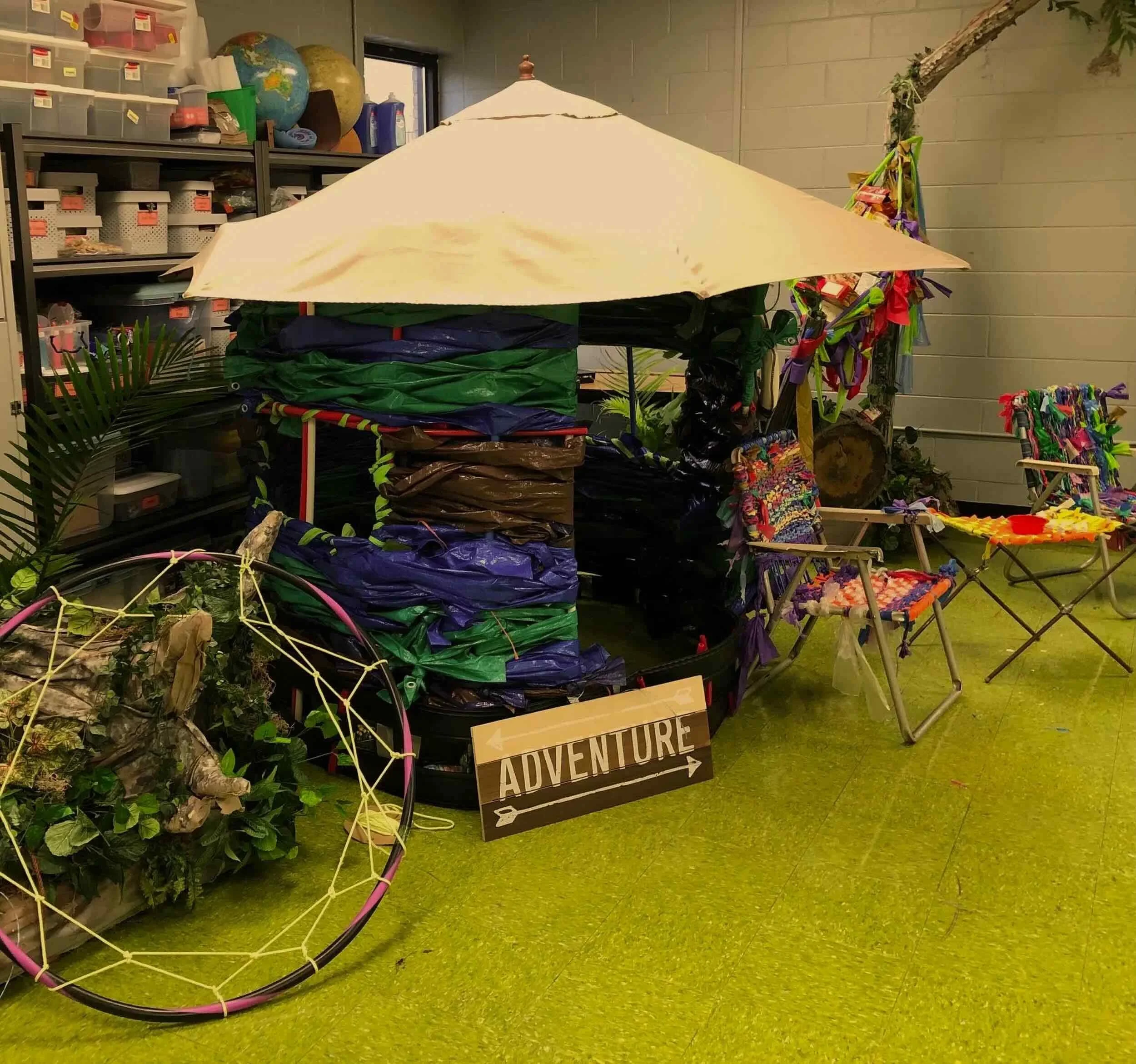 Colorful student-created installation featuring a makeshift shelter, woven chairs, and an “Adventure” sign.