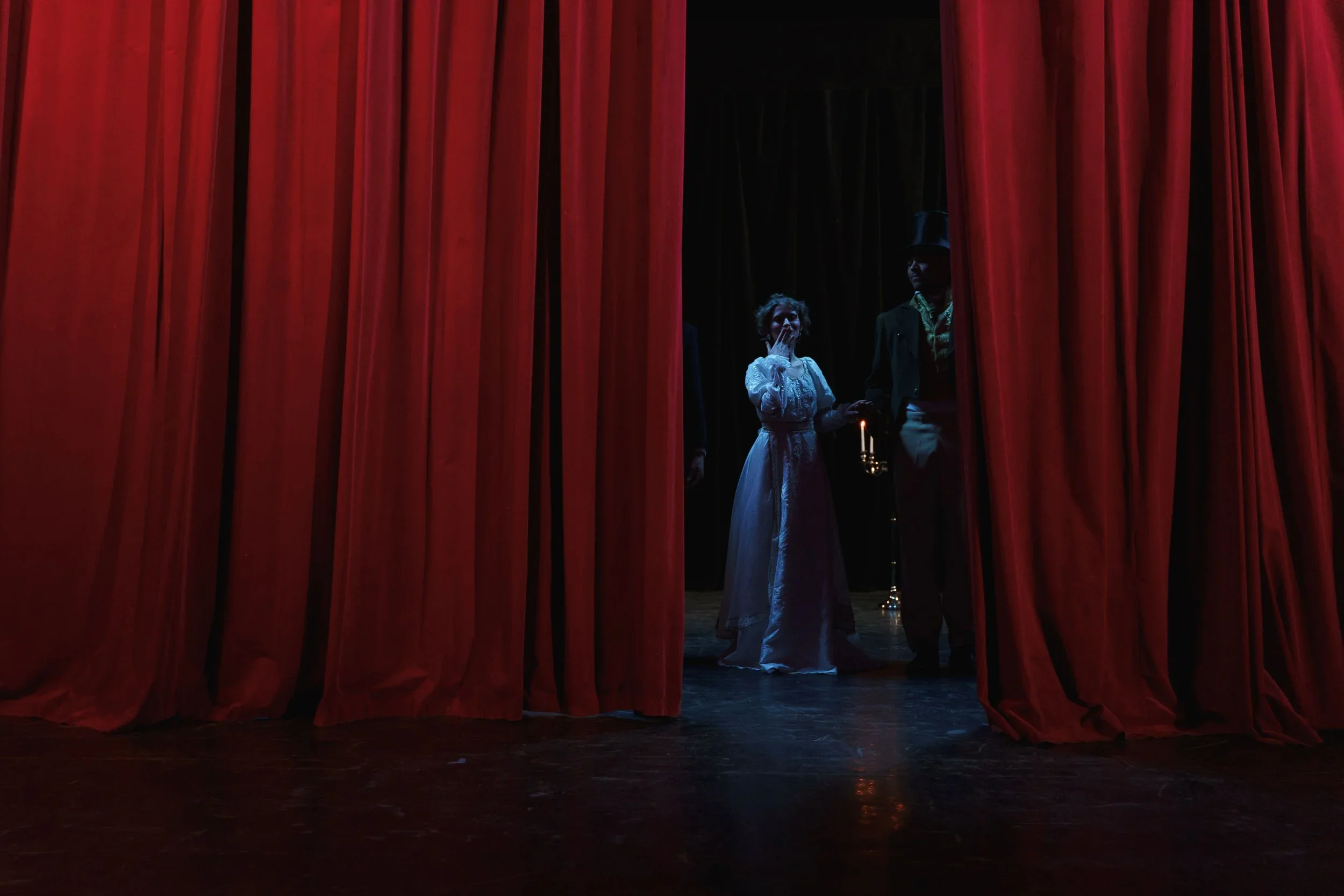 Actors after a theater performance, seen through red stage curtains with stage and black background visible.