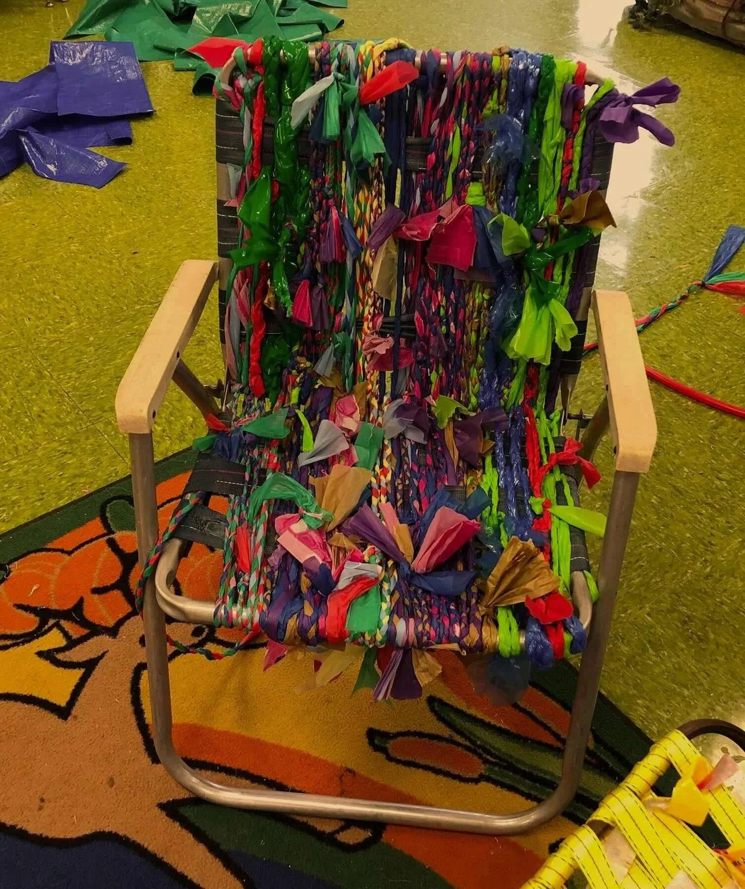Chair transformed with colorful woven and knotted materials during a collaborative arts project.