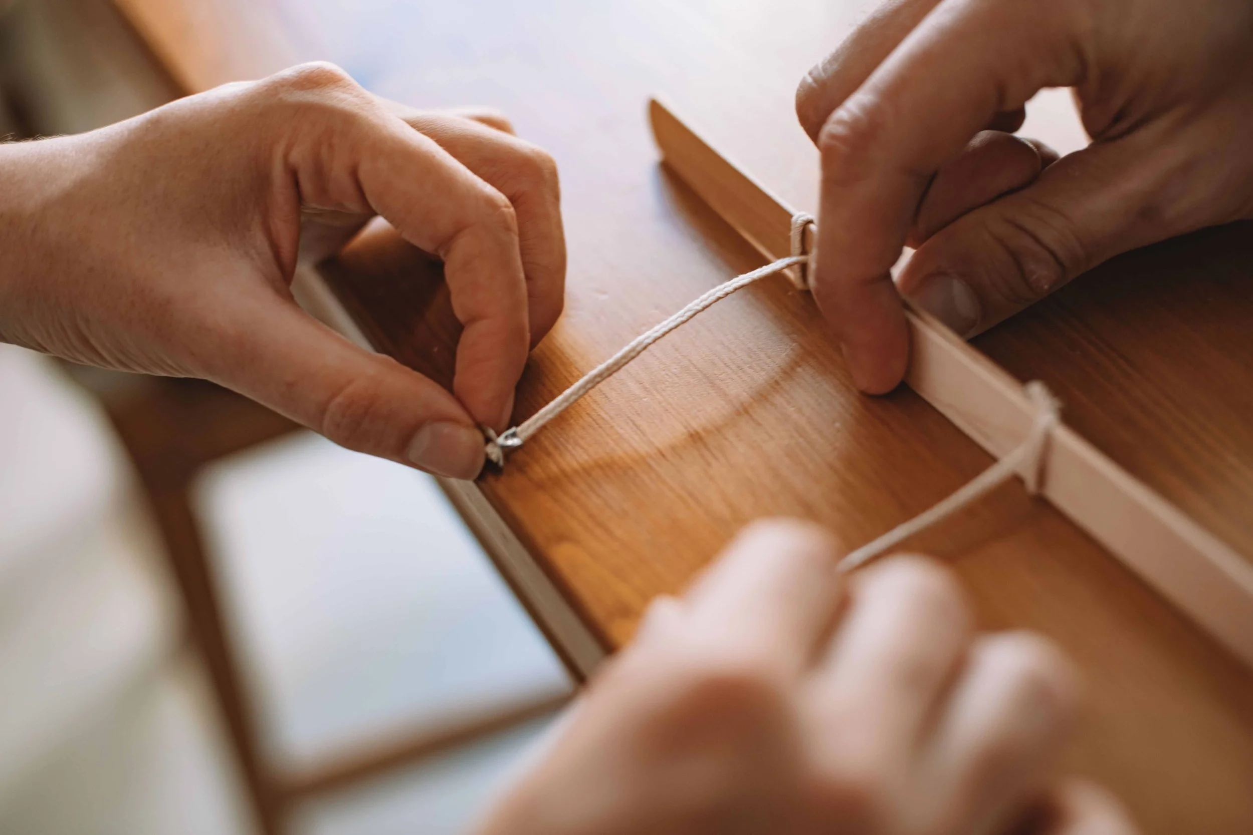Close-up of hands threading cord through a wooden board.