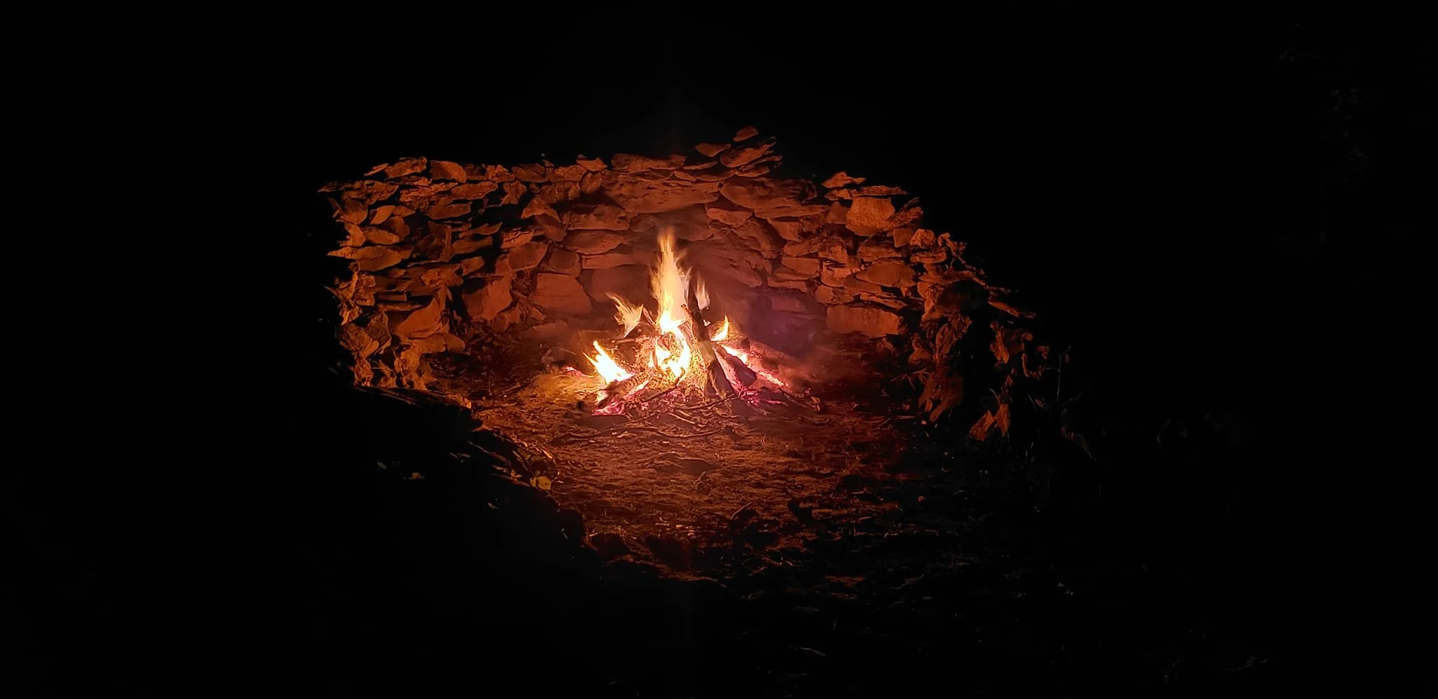 A small campfire burning in a fire pit surrounded by rocks at night.