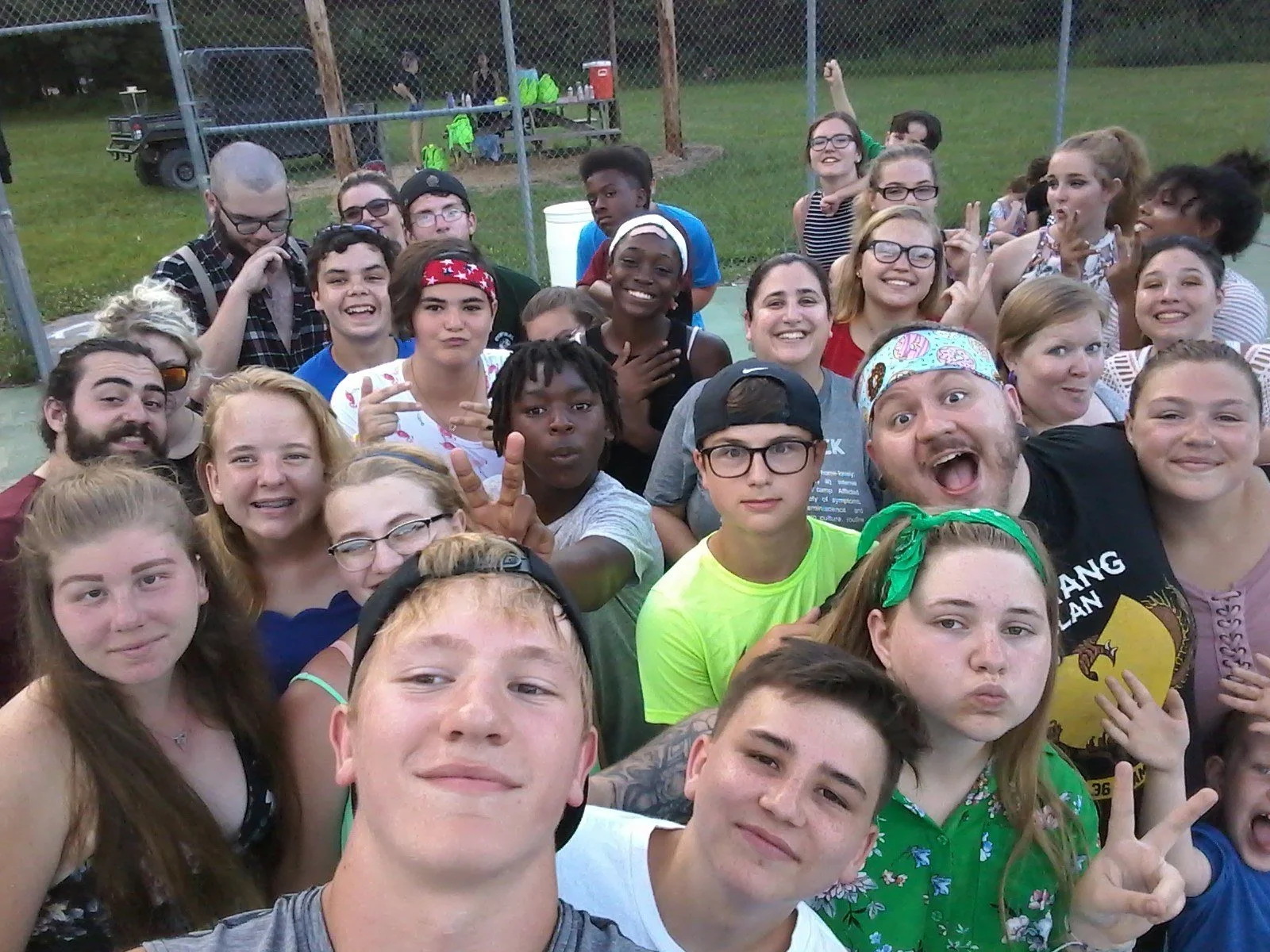 Group of smiling teenagers and young adults taking a selfie outdoors at a sports field or park