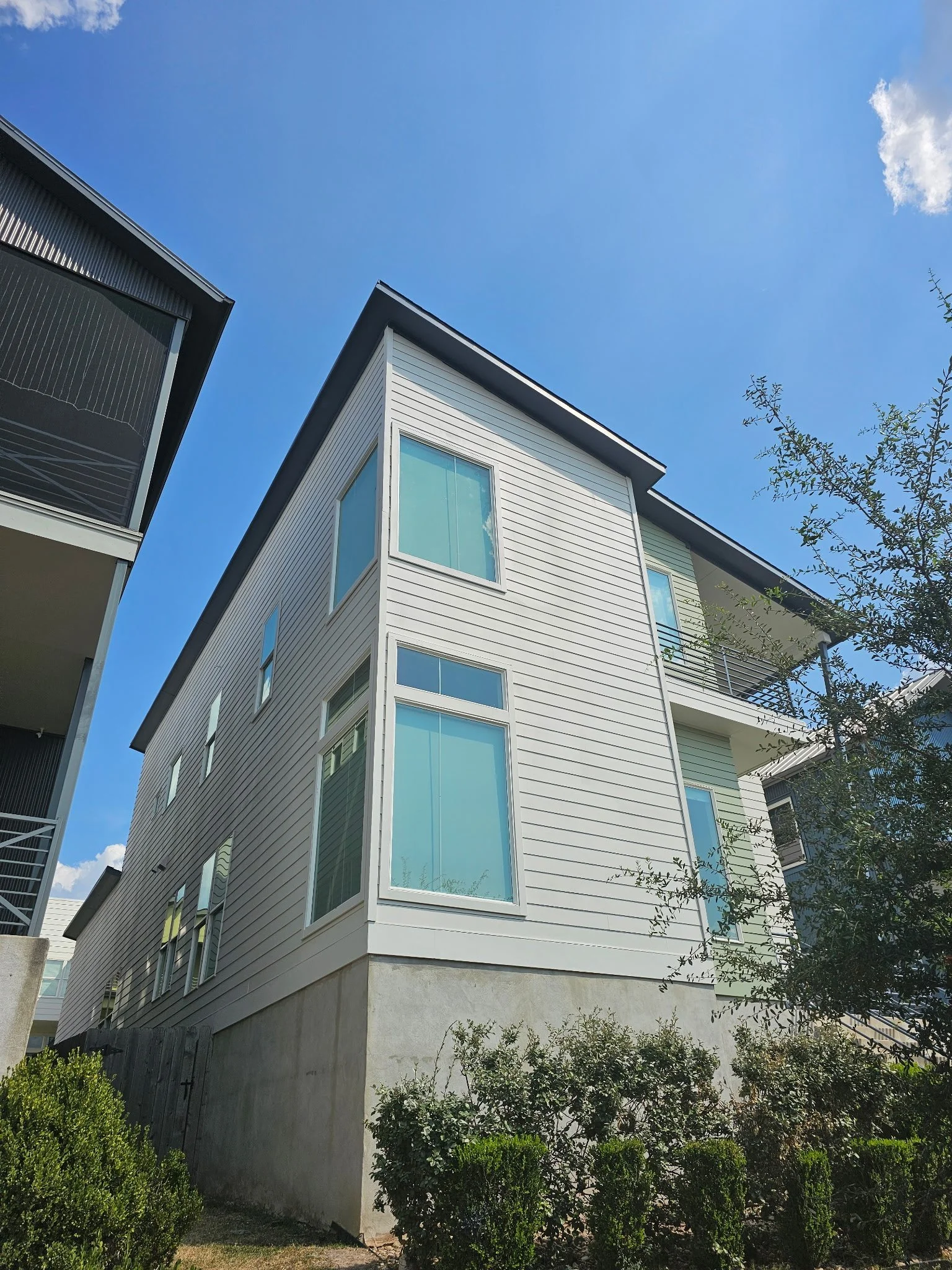 A modern multi-story building with large windows, surrounded by greenery and trees under a clear blue sky.