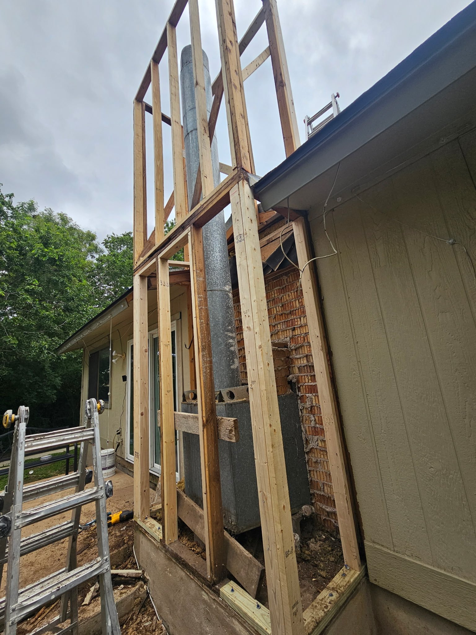 Construction site in progress showing wooden framing for a building extension, with a metal pipe and exterior wall siding visible.