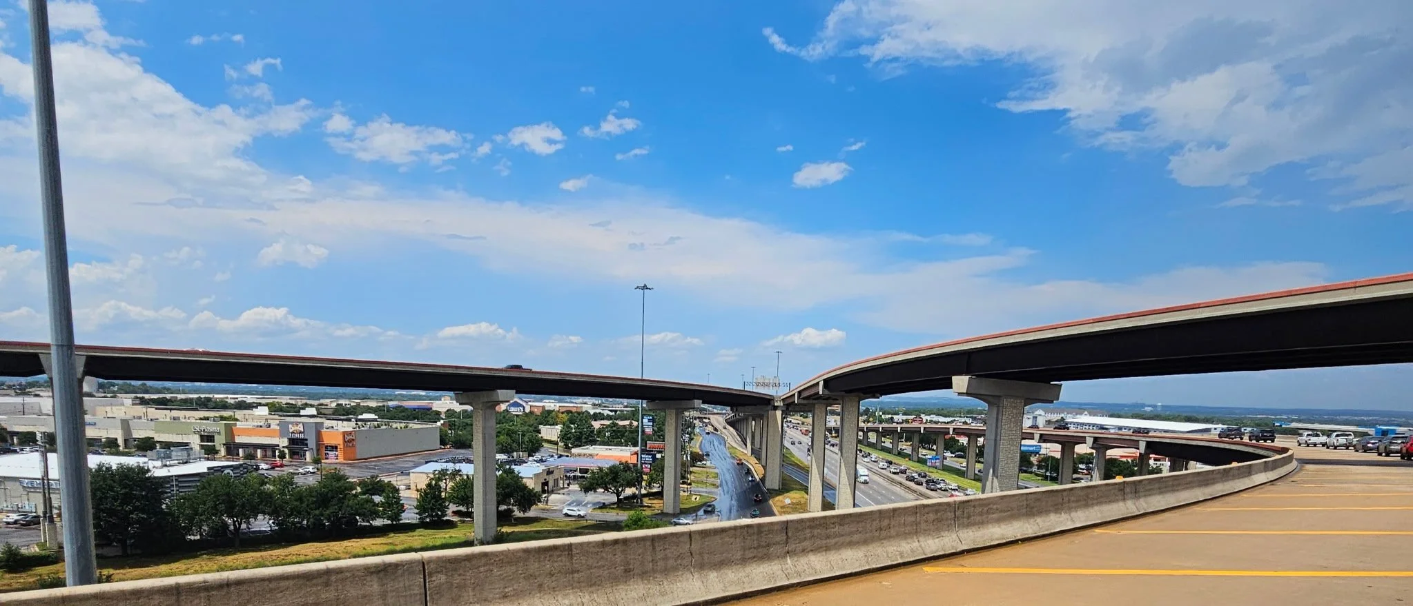 View of a multi-level highway interchange with roads, overpasses, and cars under a partly cloudy sky.