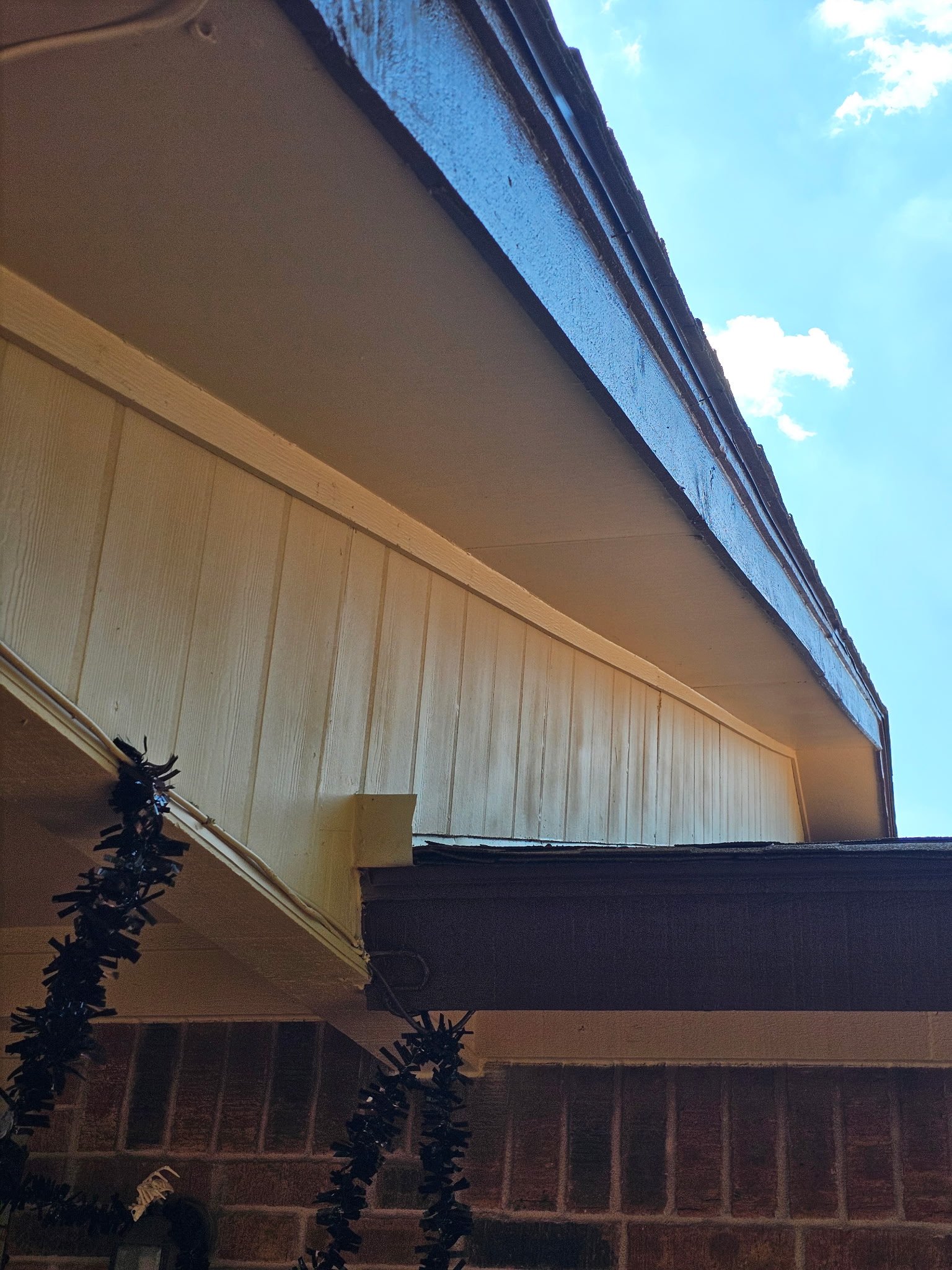 View of a building's roof and eaves from underneath, with a partly cloudy sky in the background.