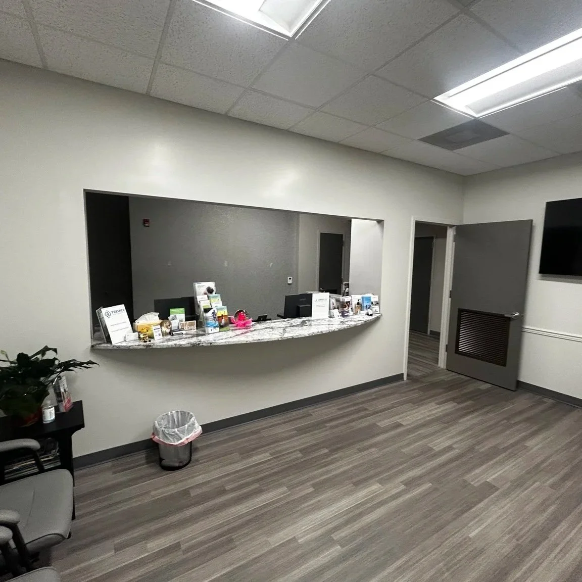 Indoor reception area with a curved marble counter, a small trash bin, chairs, and computer monitors on the counter.