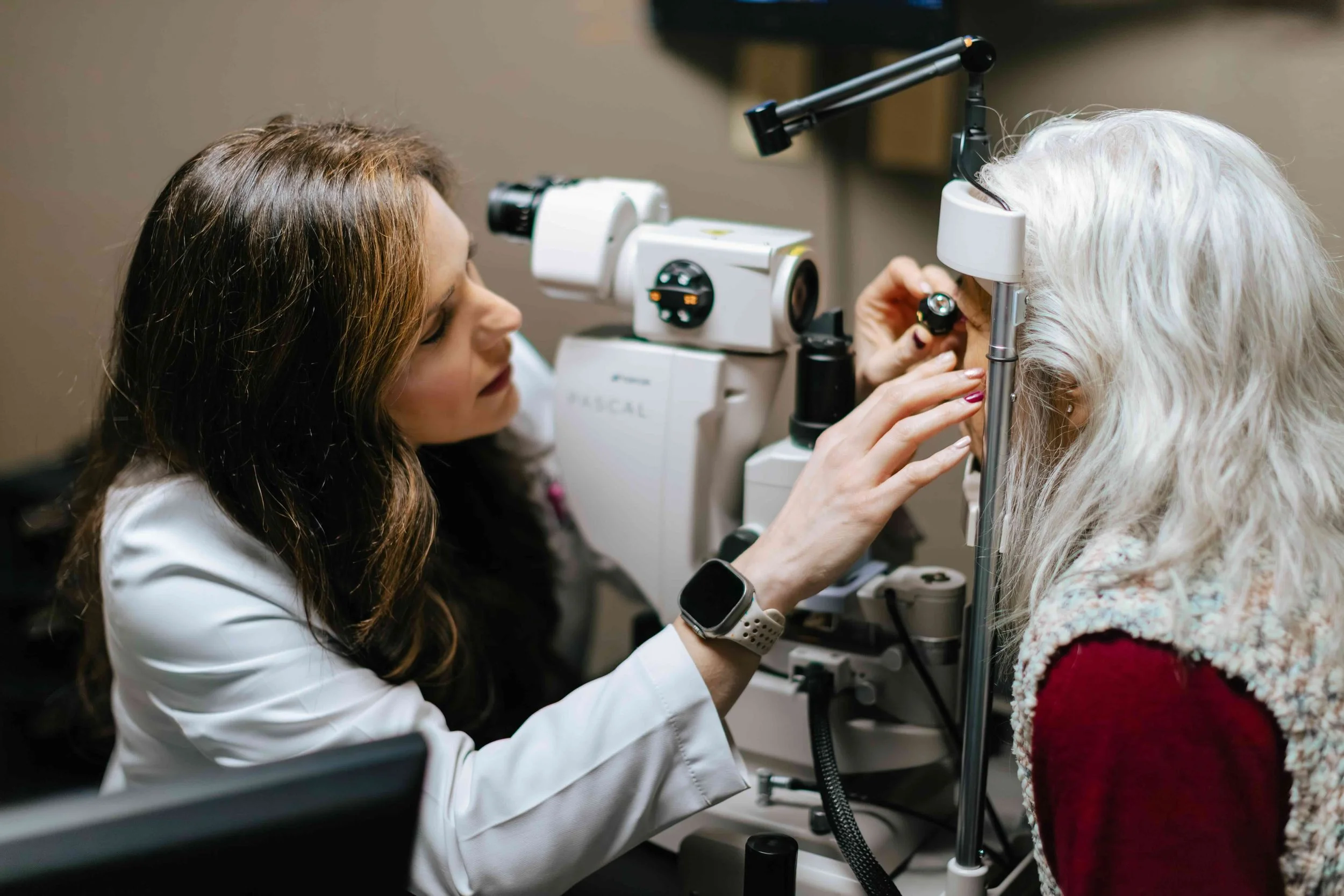 An eye doctor examines an elderly woman's eye using specialized equipment in a clinic.