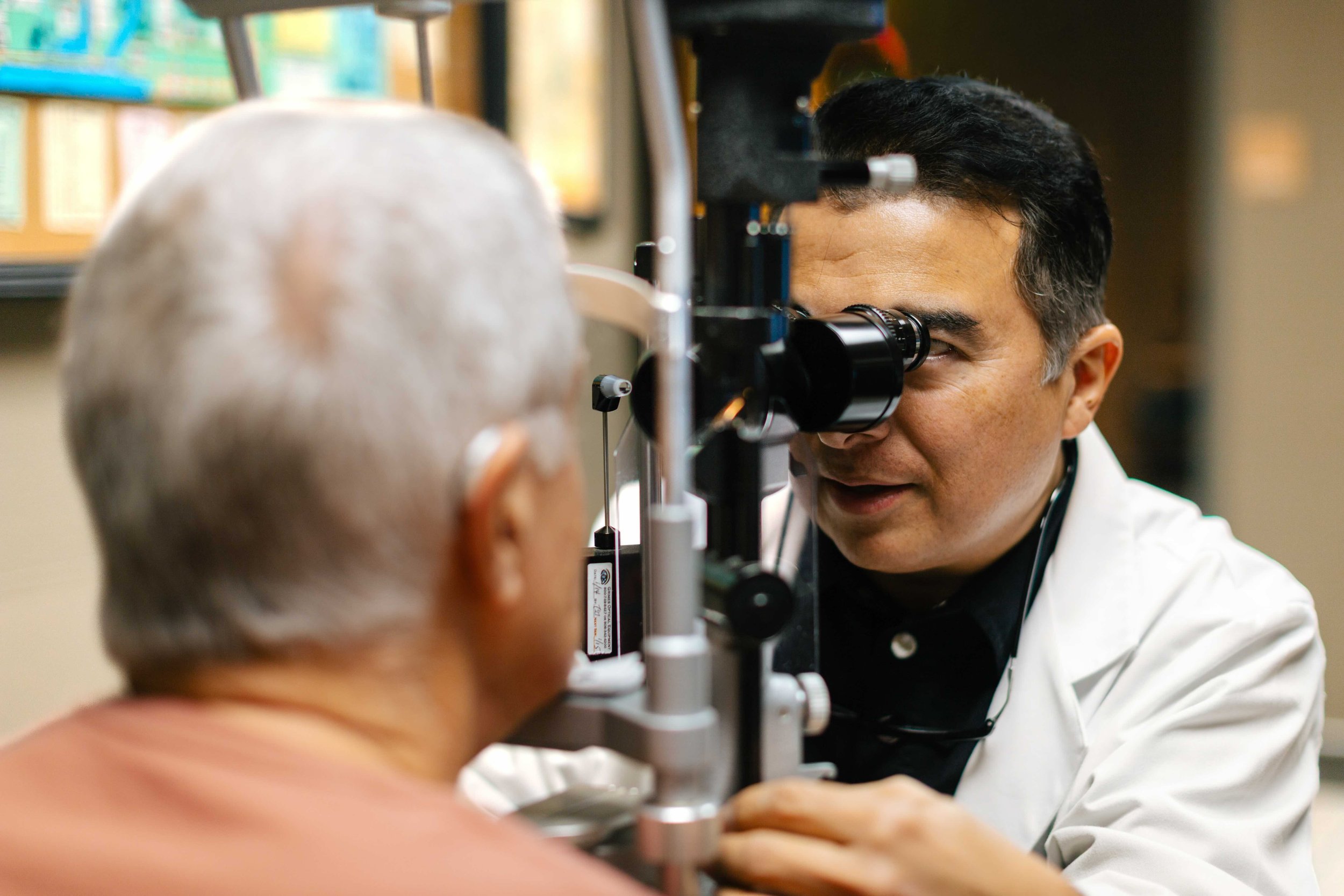A male retina specialist using a slit lamp to examine an elderly patient's eyes in a clinical setting.