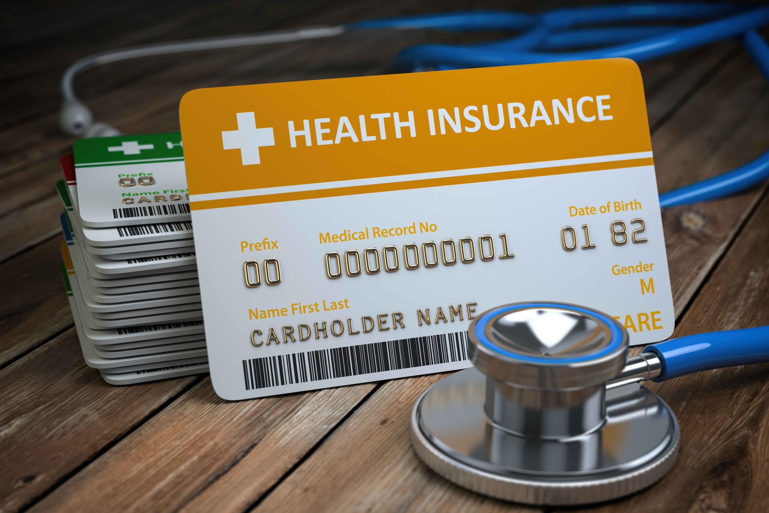 Stack of insurance cards, prominently displaying a health insurance card with a gold stripe, barcode, and personal details, alongside a stethoscope and medical equipment on a wooden surface.