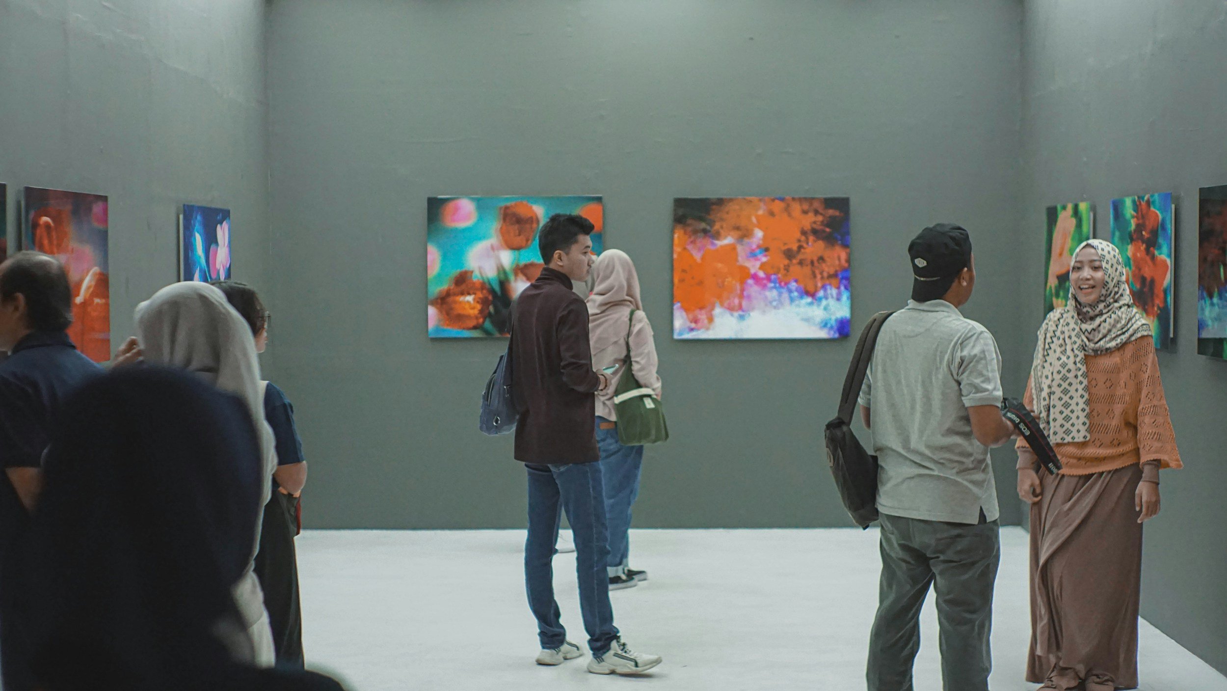 People viewing colorful abstract paintings in an art gallery.