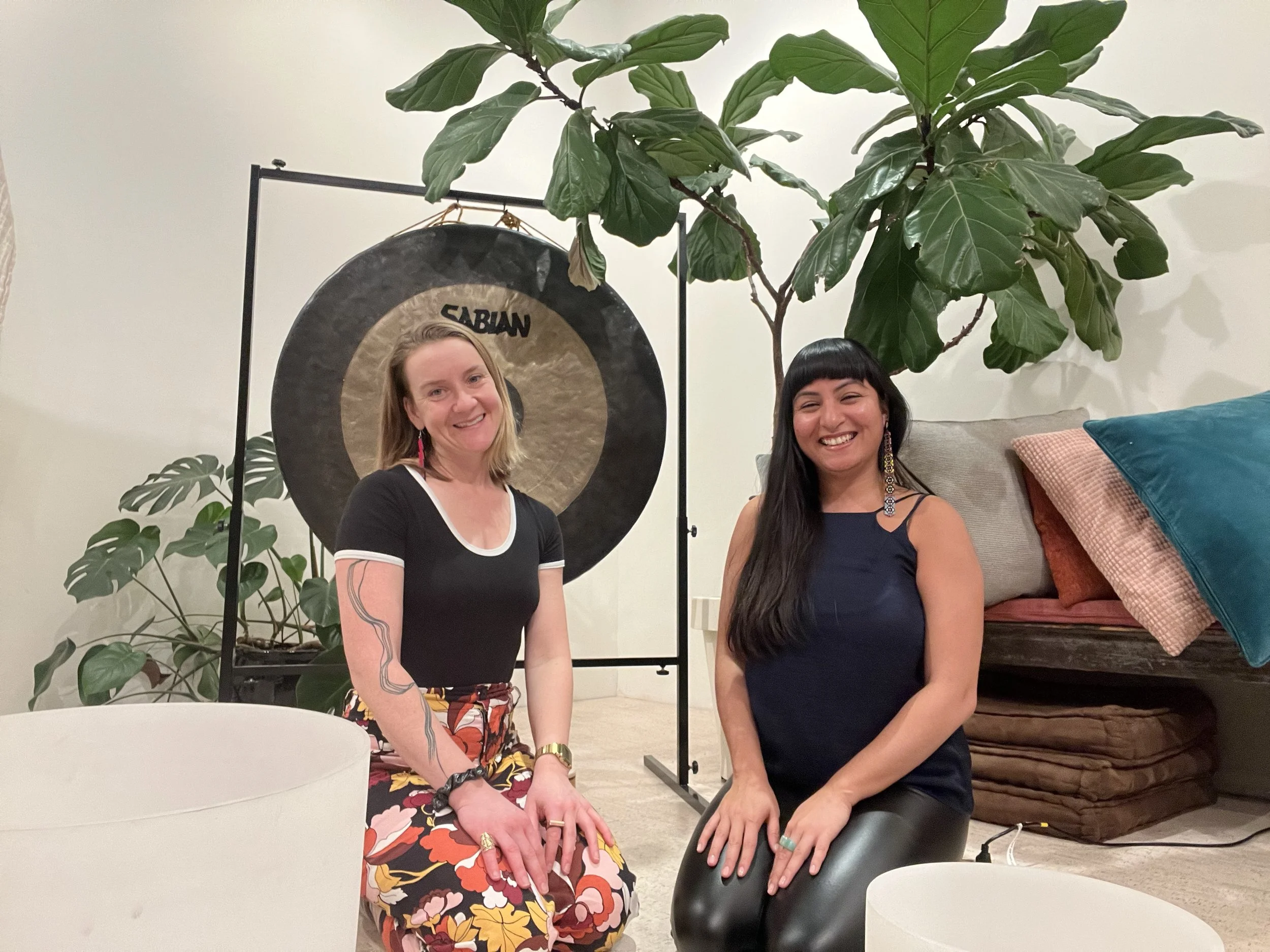 Two creative arts therapists who provide ketamine therapy in Brooklyn kneeling in a space with crystal bowls. plants and a gong. The ketamine group starts in September 2026 and application are open now. Hosted by LCATs Laura Foxx and Juanita Viera
