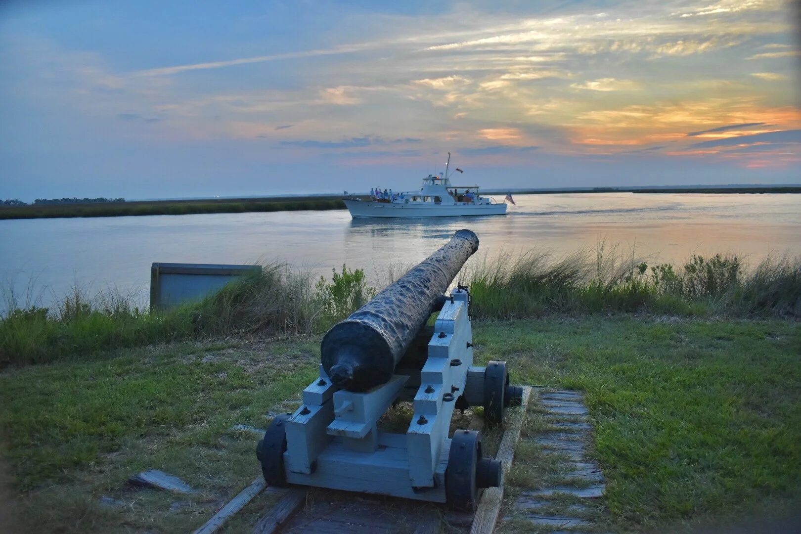 String of Pearls yacht cruising past a historic cannon on the marsh at sunset