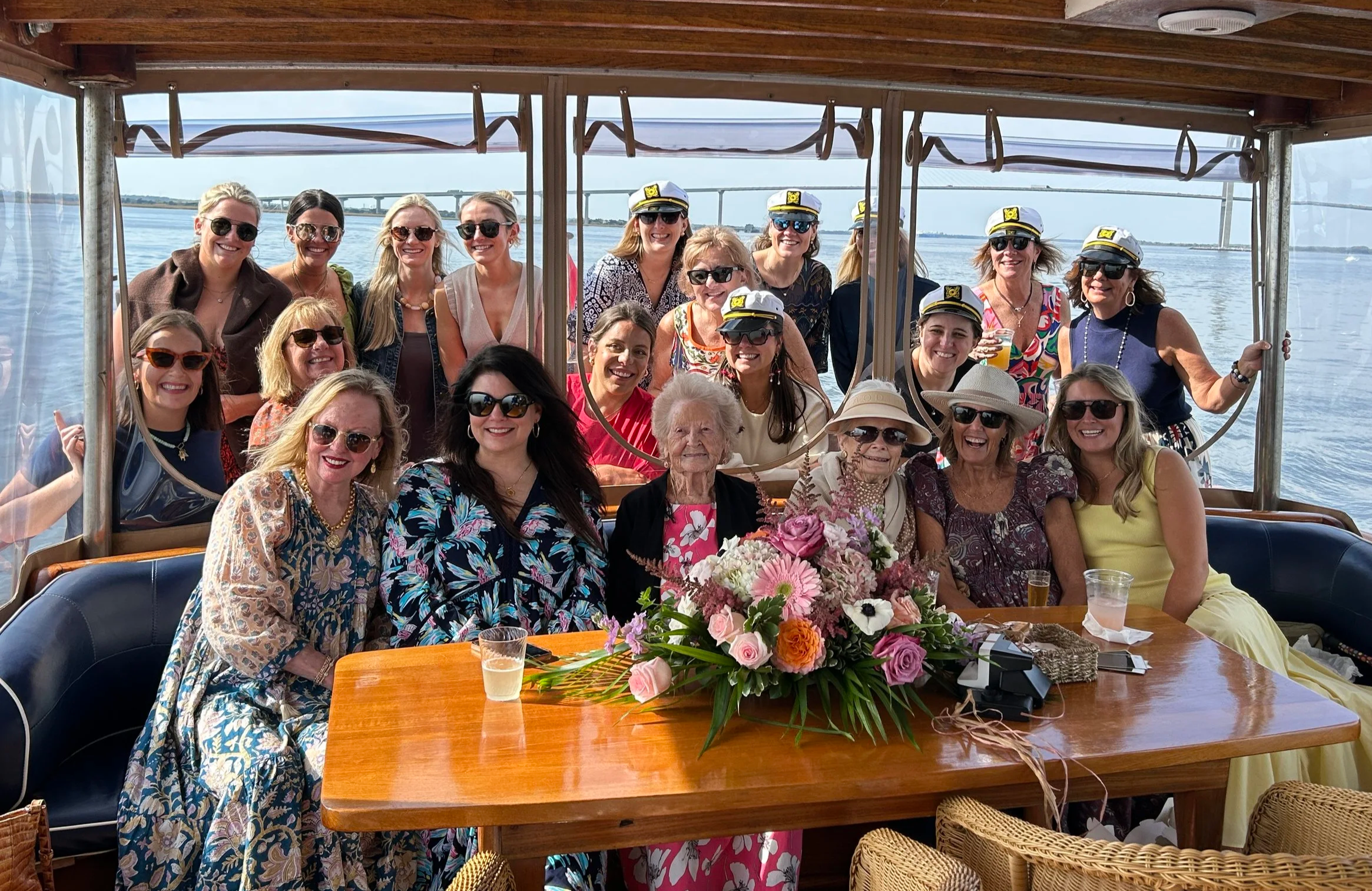 Group of women gathered around the wooden table on the yacht's covered aft deck, with a bouquet of flowers