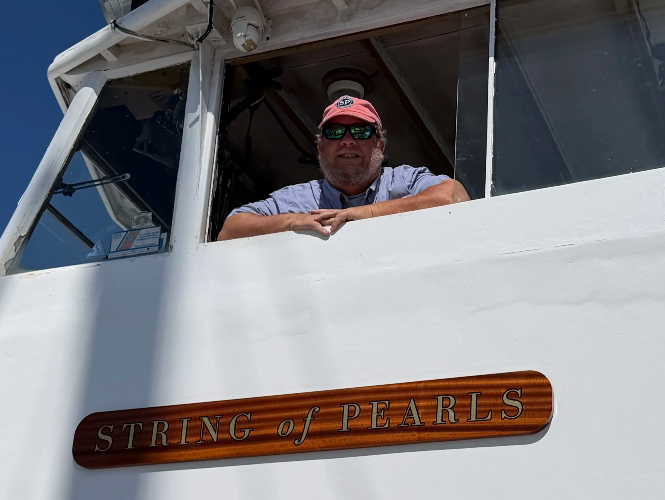 Captain looking out from the yacht's bridge window above the String of Pearls name board