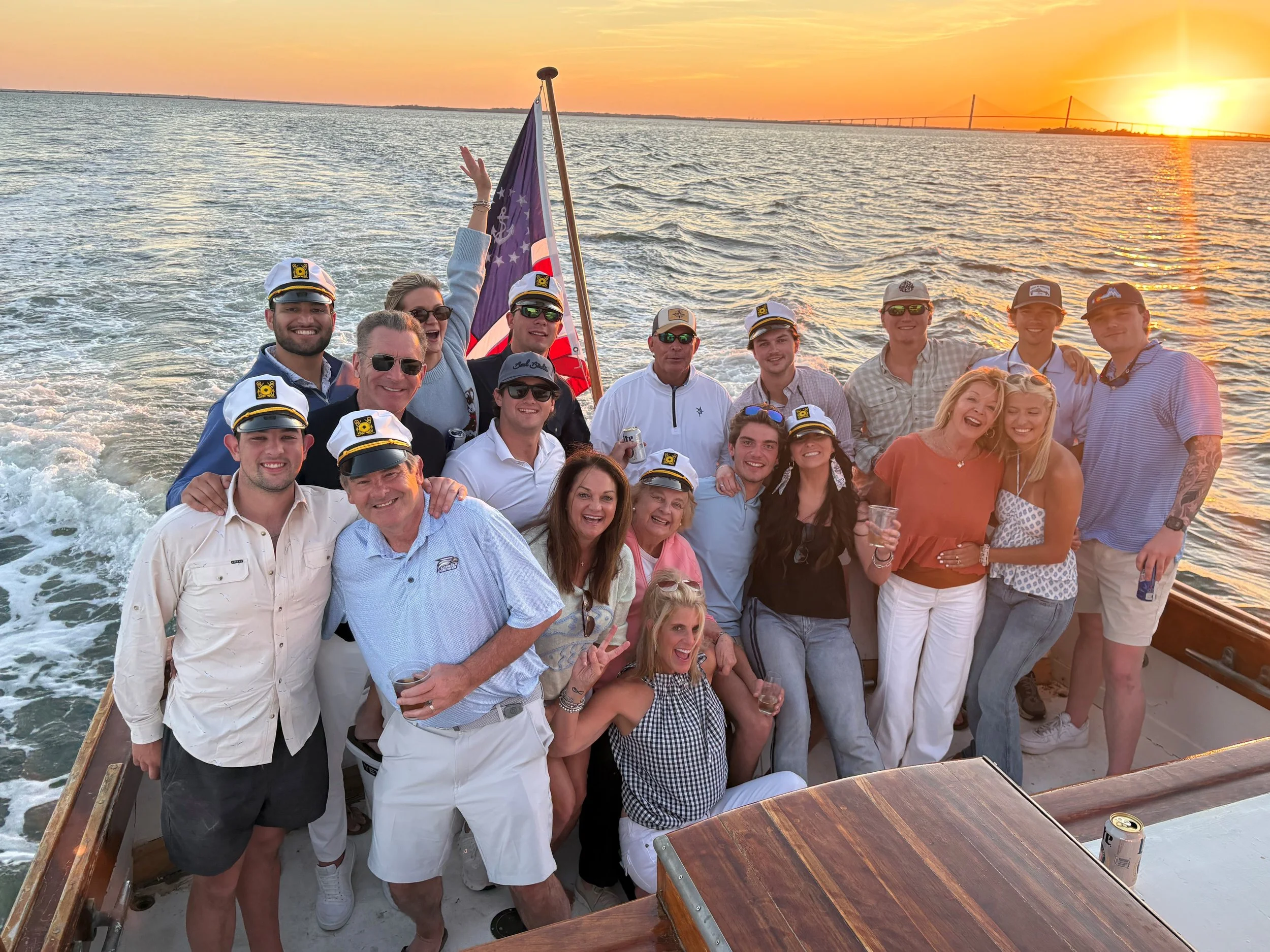 Group of guests, some in captain hats, posing on the yacht deck at sunset