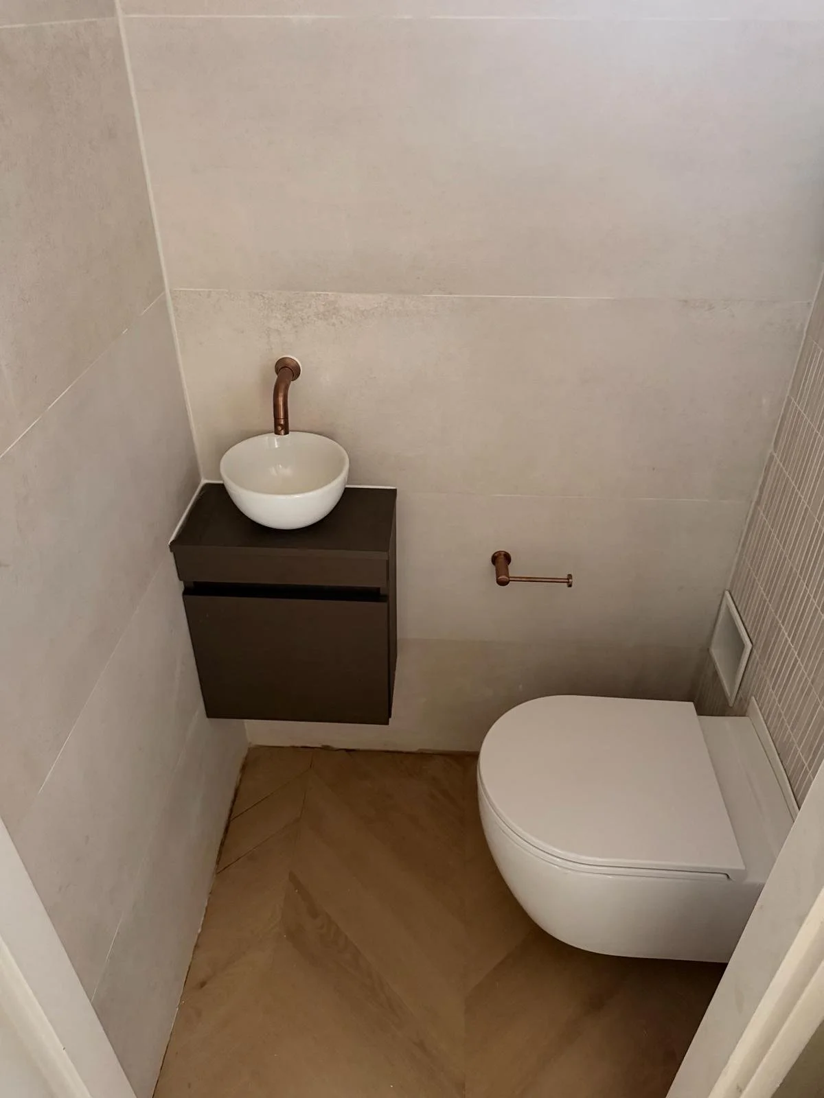 Een kleine badkamer met een hangend toilet en een wandgemonteerd wasbakje met een koperen kraan.