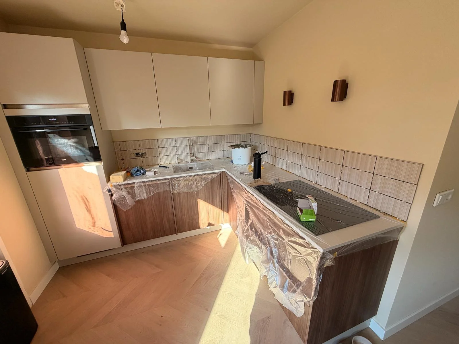 Kleine keuken onder renovatie met plastic afdekking op werkbladen, onvoltooide tegels en keukenapparatuur.