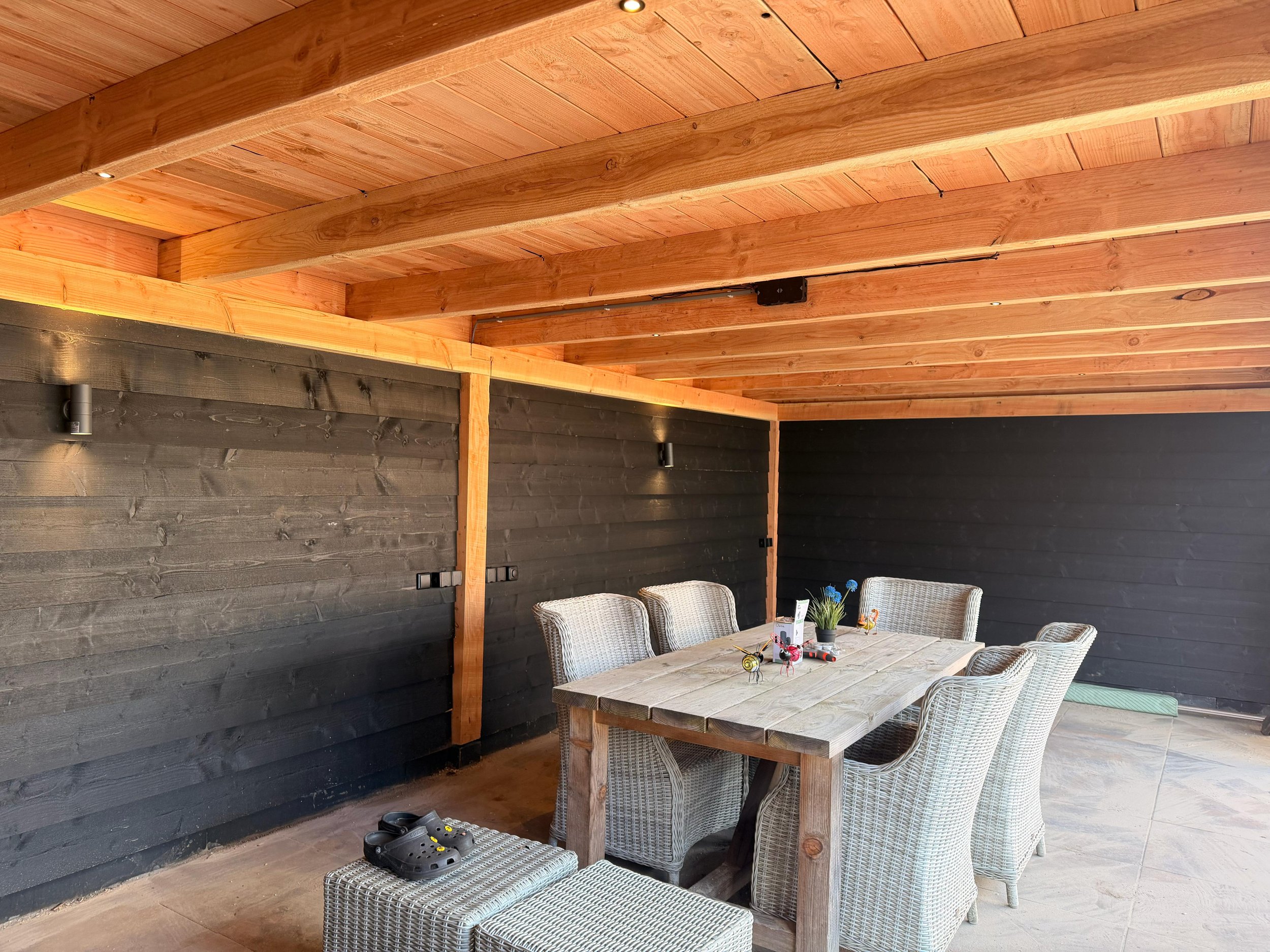 Buiten eetgedeelte met houten tafel en wicker stoelen onder een houten terrasoverkapping.