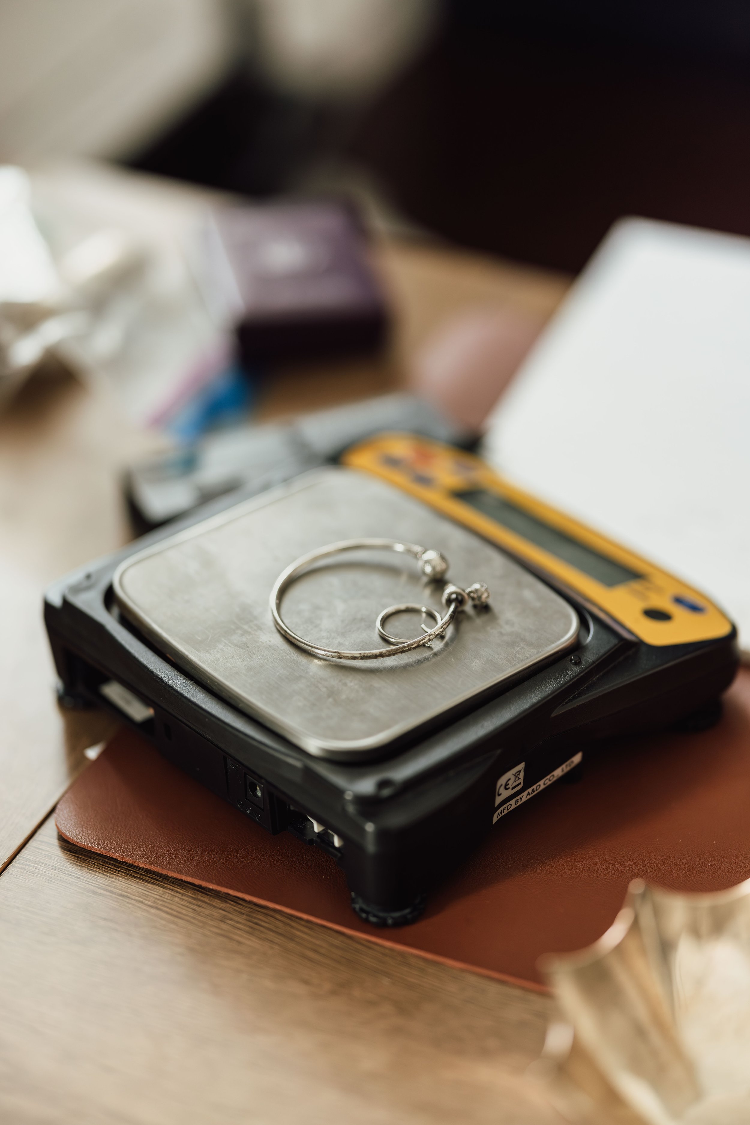 A close-up view of a small jewelry display tray with silver hoop earrings on it, placed on a black electronic device, likely a hard drive or portable speaker, on top of a brown leather surface.