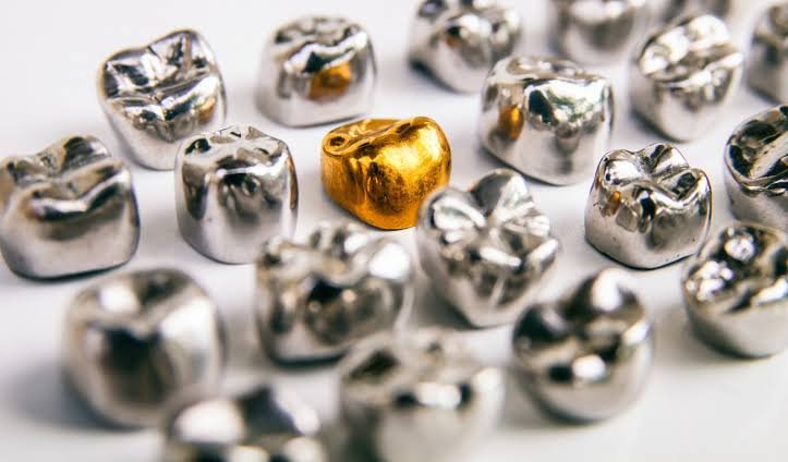 Close-up of several metallic gold and silver dental crowns, with one gold crown standing out among the silver ones.