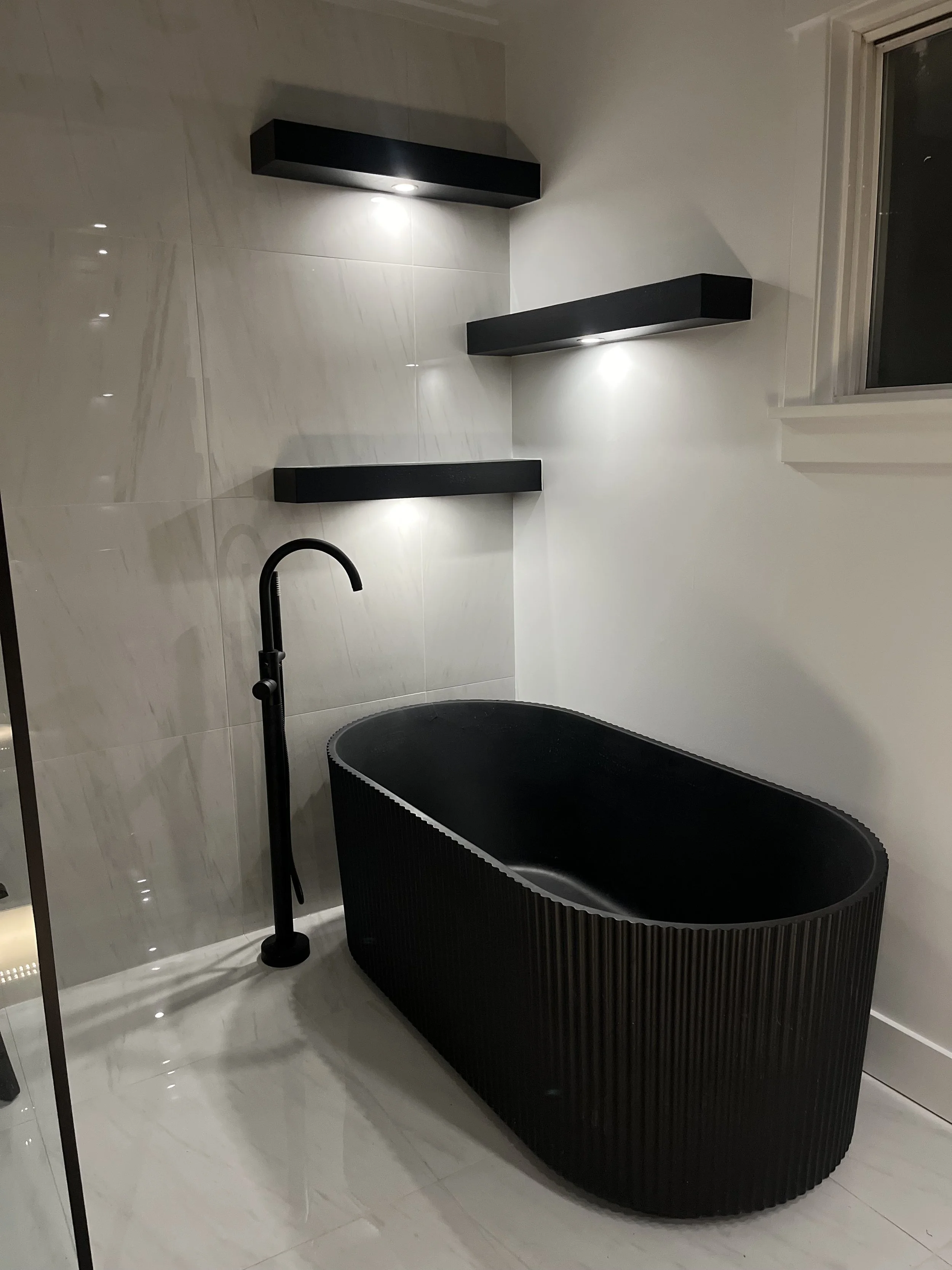 Modern bathroom featuring a black freestanding bathtub with vertical ridges, black floor-standing faucet, and white marble tiled walls.