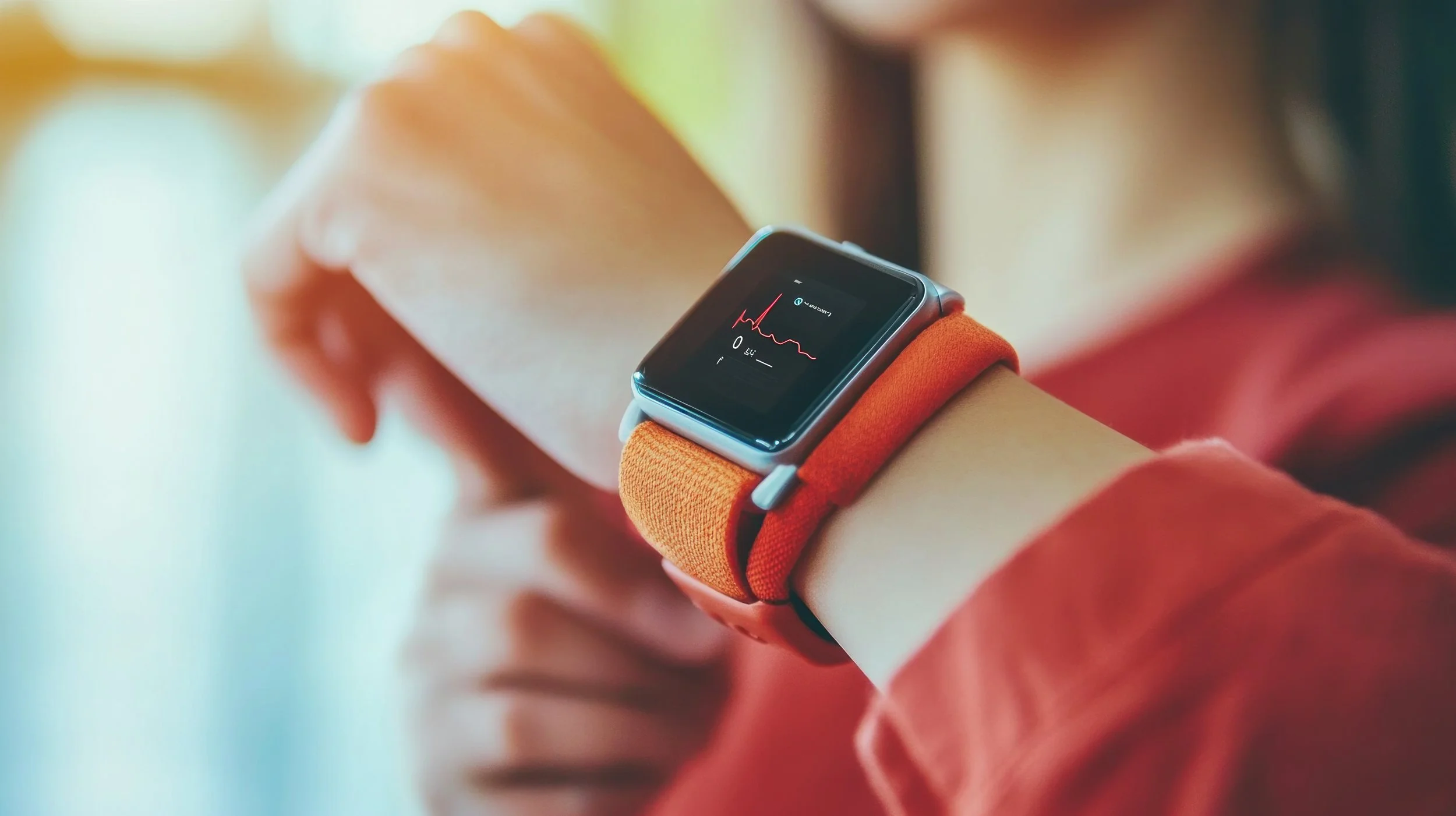A person wearing an orange wristband and a smartwatch displaying a heart rate graph with fluctuations.