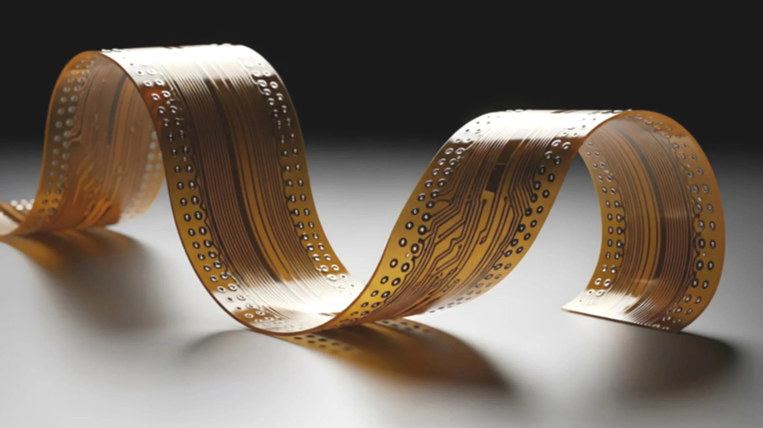 A close-up of a flexible circuit board with electronic components, curled into a loop against a dark background.