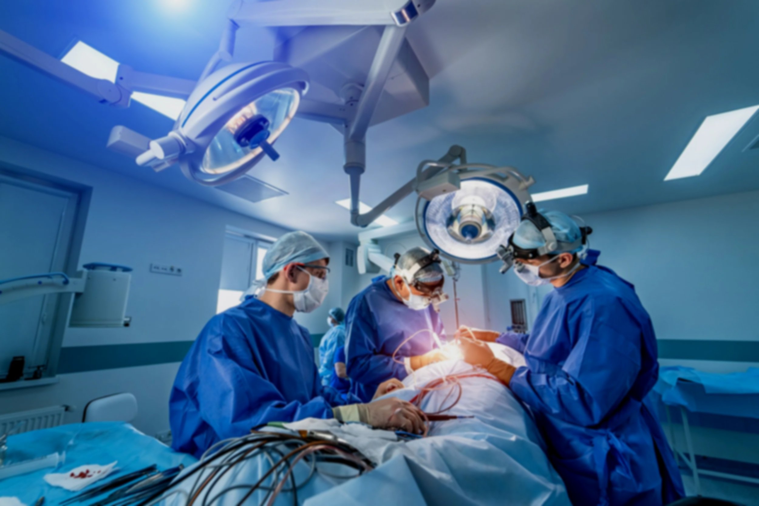 A group of surgeons performing a medical operation in an operating room, with surgical lights overhead and medical equipment on the table.