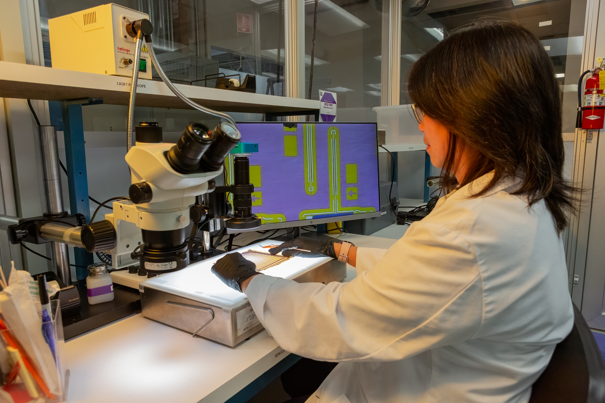 A scientist in a white lab coat working with a microscope and electronic equipment in a laboratory.