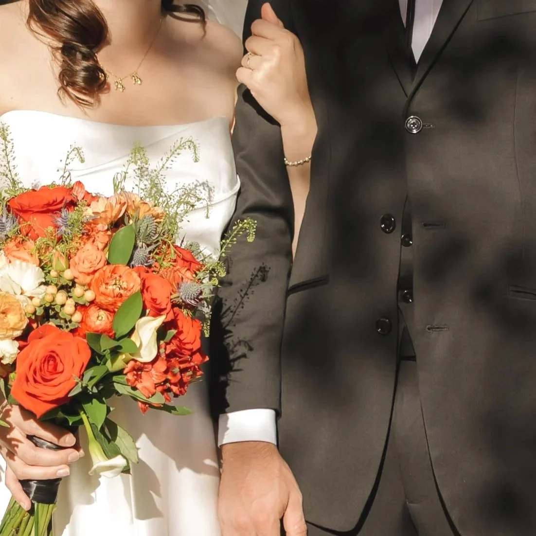 Close-up of a bride holding a bouquet of orange and white flowers standing with a groom dressed in a dark suit during a wedding ceremony.