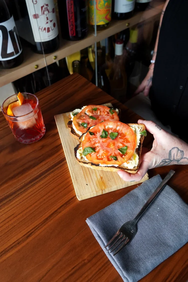 Two slices of Elmore Mountain Bread topped with sliced tomatoes, fresh basil, and a ricotta spread served with a Negroni