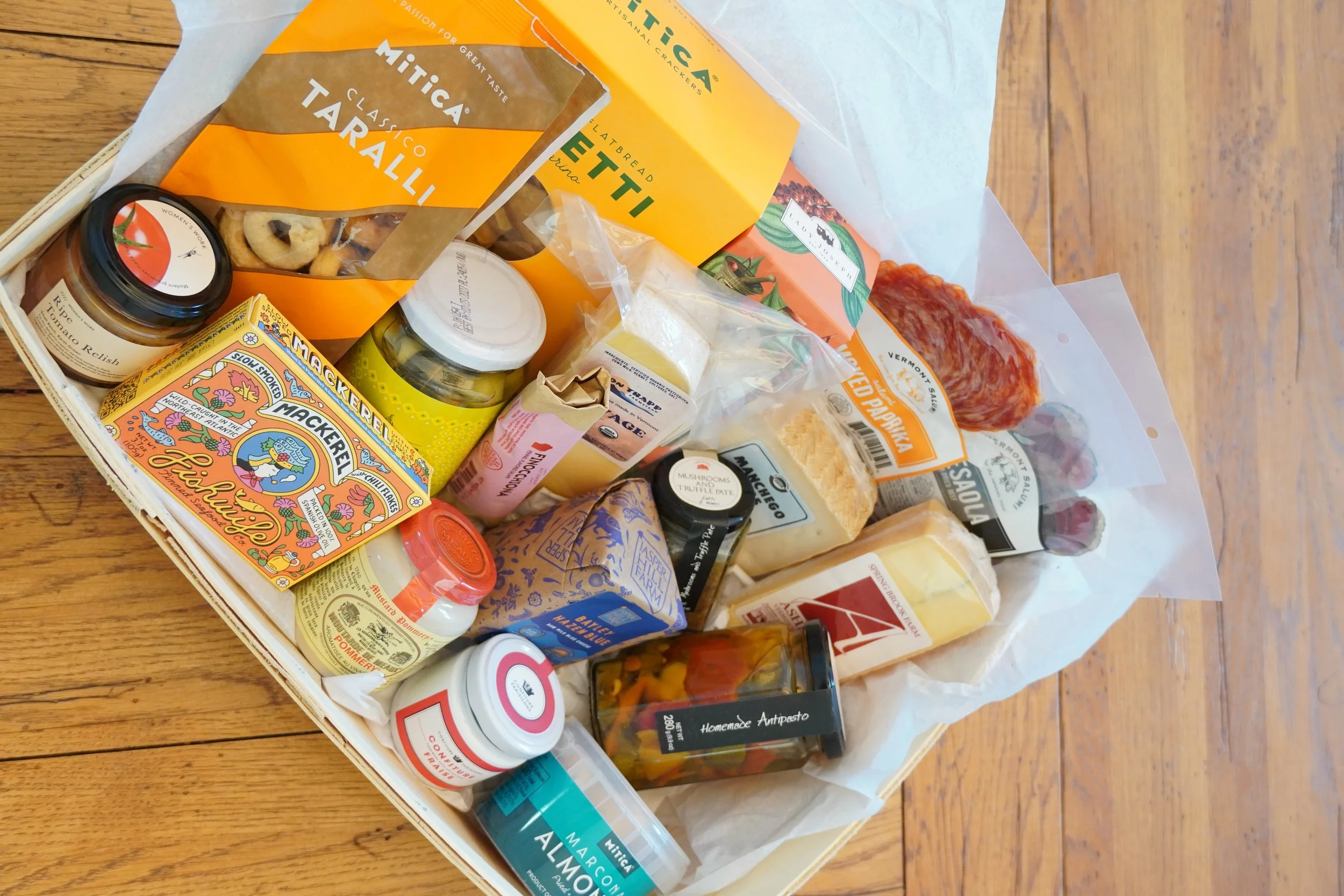 A gift basket filled with gourmet food items including Italian crackers, tomato relish, cheese, cured meats, and condiments from Cork Market in Stowe, Vermont. Find all the best gifts and homewares all in one place.