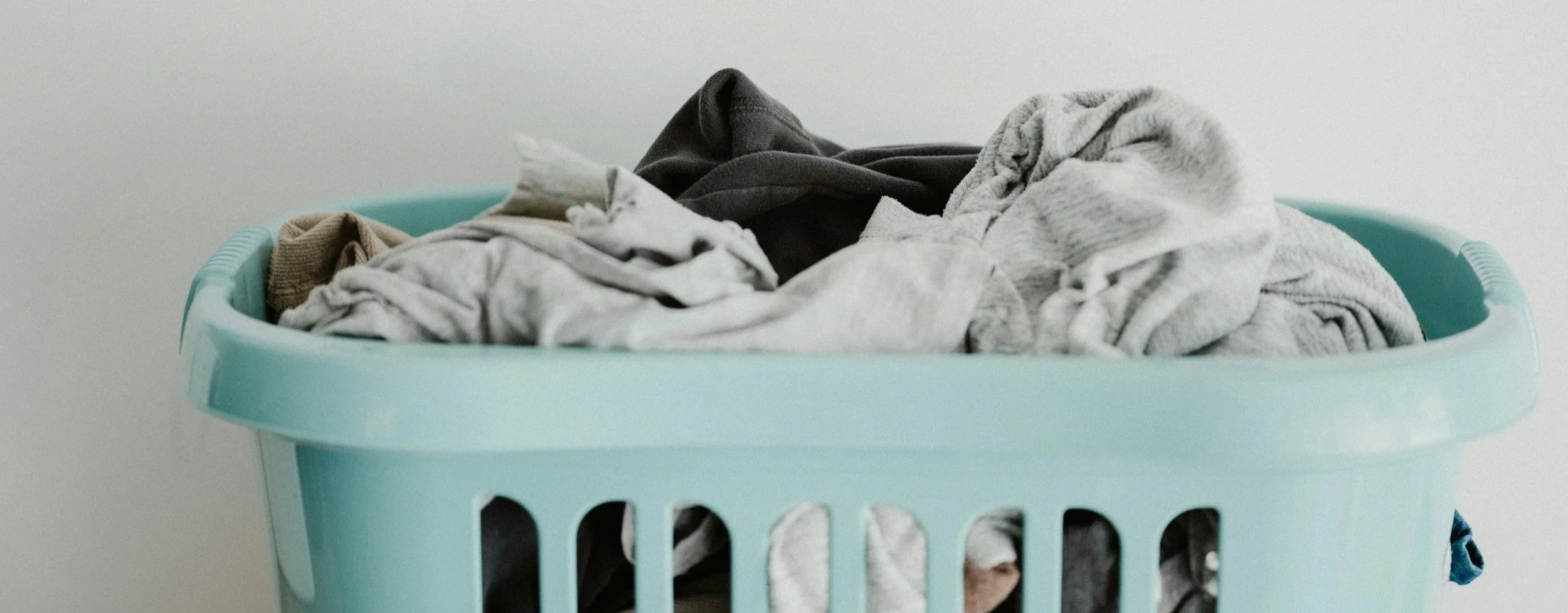 Blue laundry basket filled with clothing infront of a white wall.