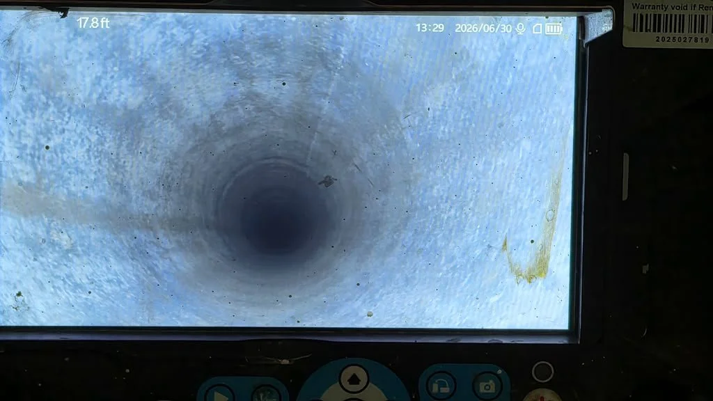A computer screen shows a view of the inside of a pipe or well, looking downward into a dark, cylindrical space with some dirt and debris visible.
