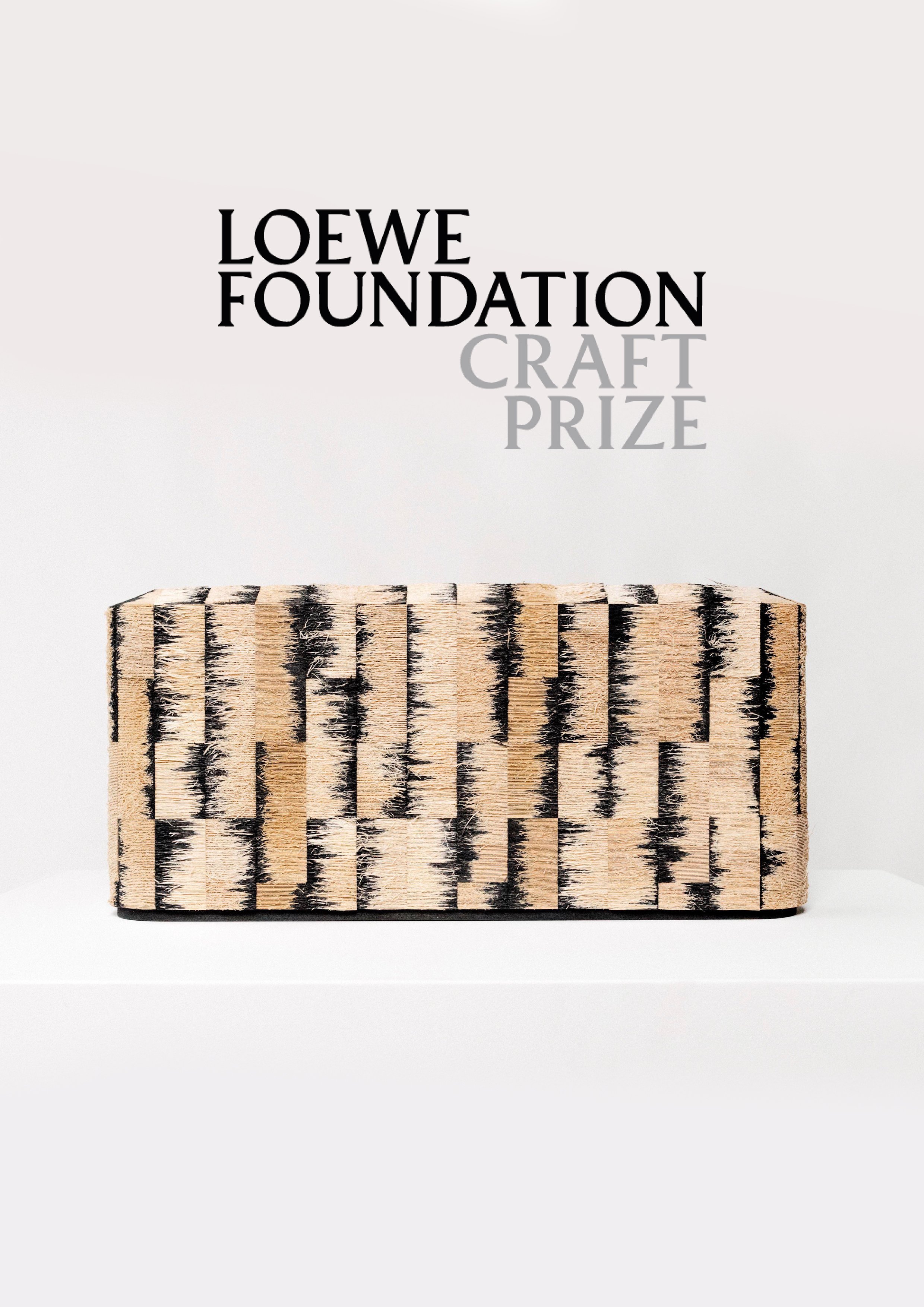 A wooden block with black and beige patterns on its surface, placed on a white surface against a light background. Text overlay reads 'LOEWE FOUNDATION CRAFT PRIZE' in black and gray font.