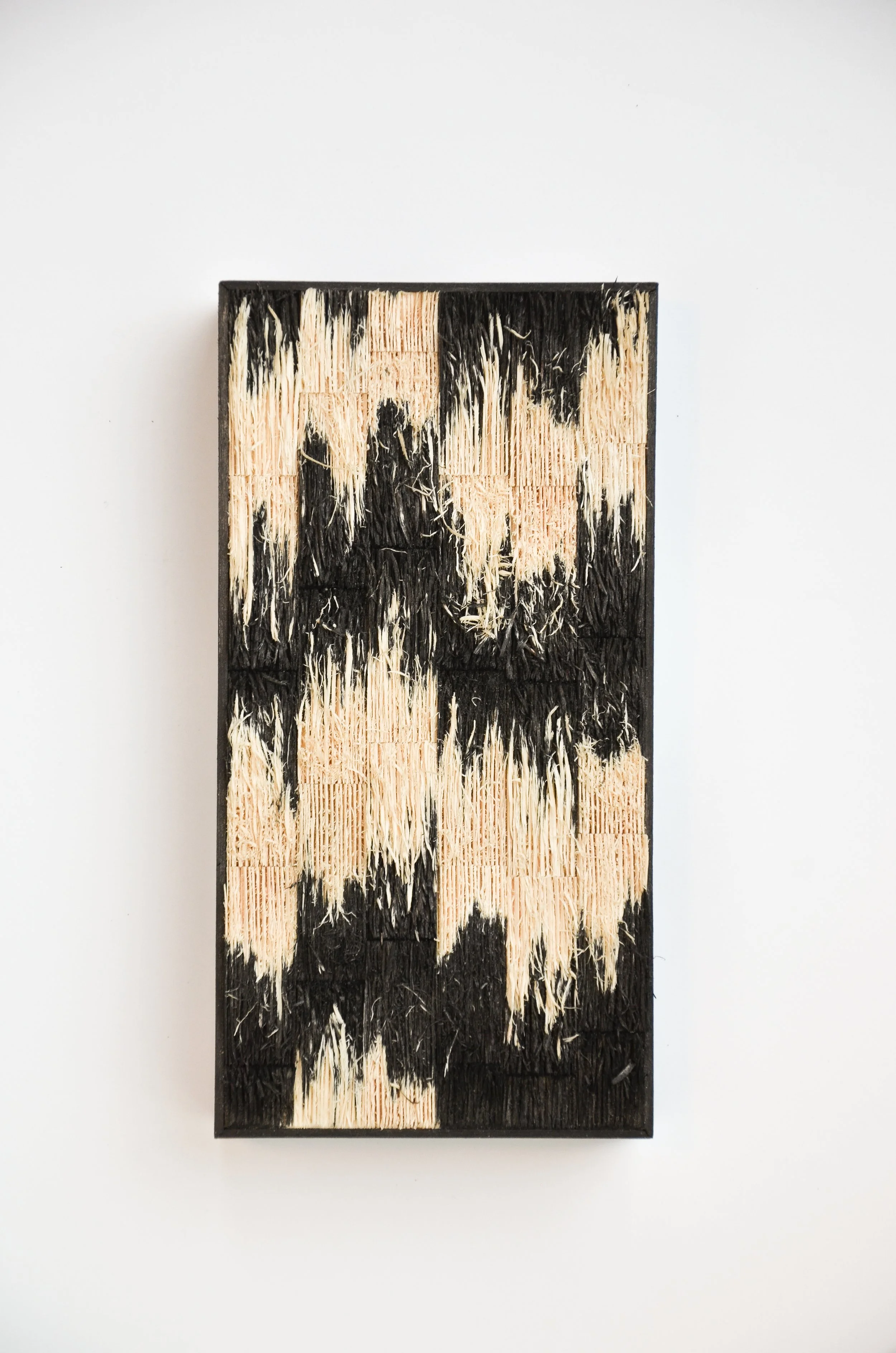 Painted wooden panel with beige and black streaks, mounted on a white wall.