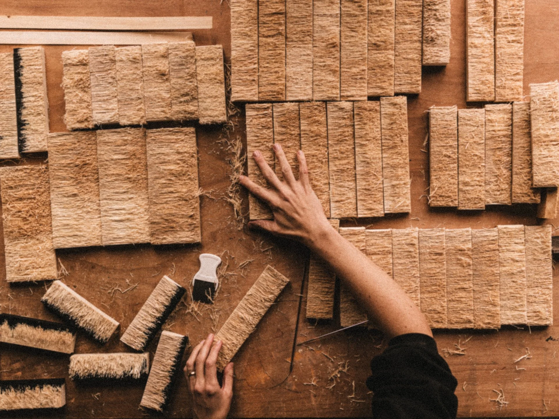Close-up of a person assembling wooden blocks on a work surface, with various wood pieces and tools scattered around.
