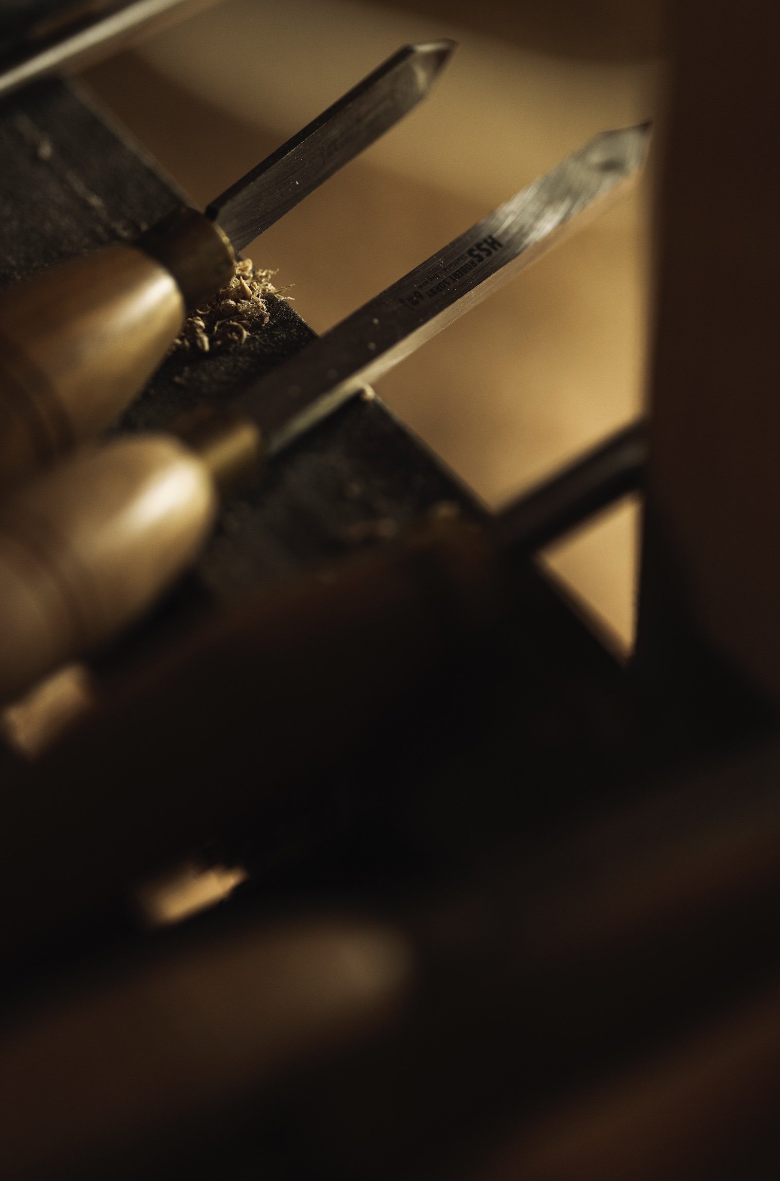 Close-up of two metallic chisels placed on a wooden surface, with wood shavings around them.