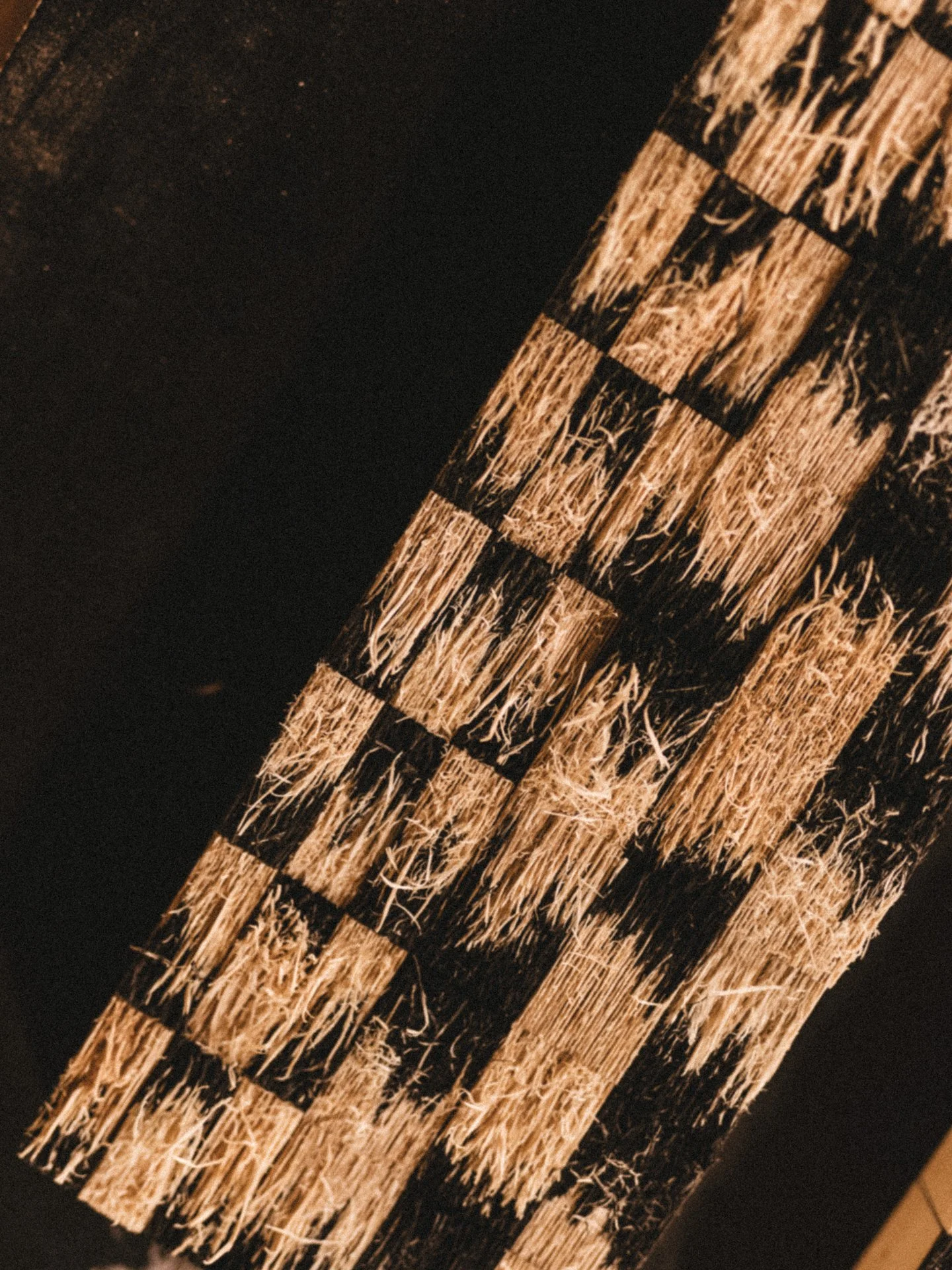 A close-up of a wooden surface with a pattern of dark and light rectangular sections, showing the texture of the wood and grain.