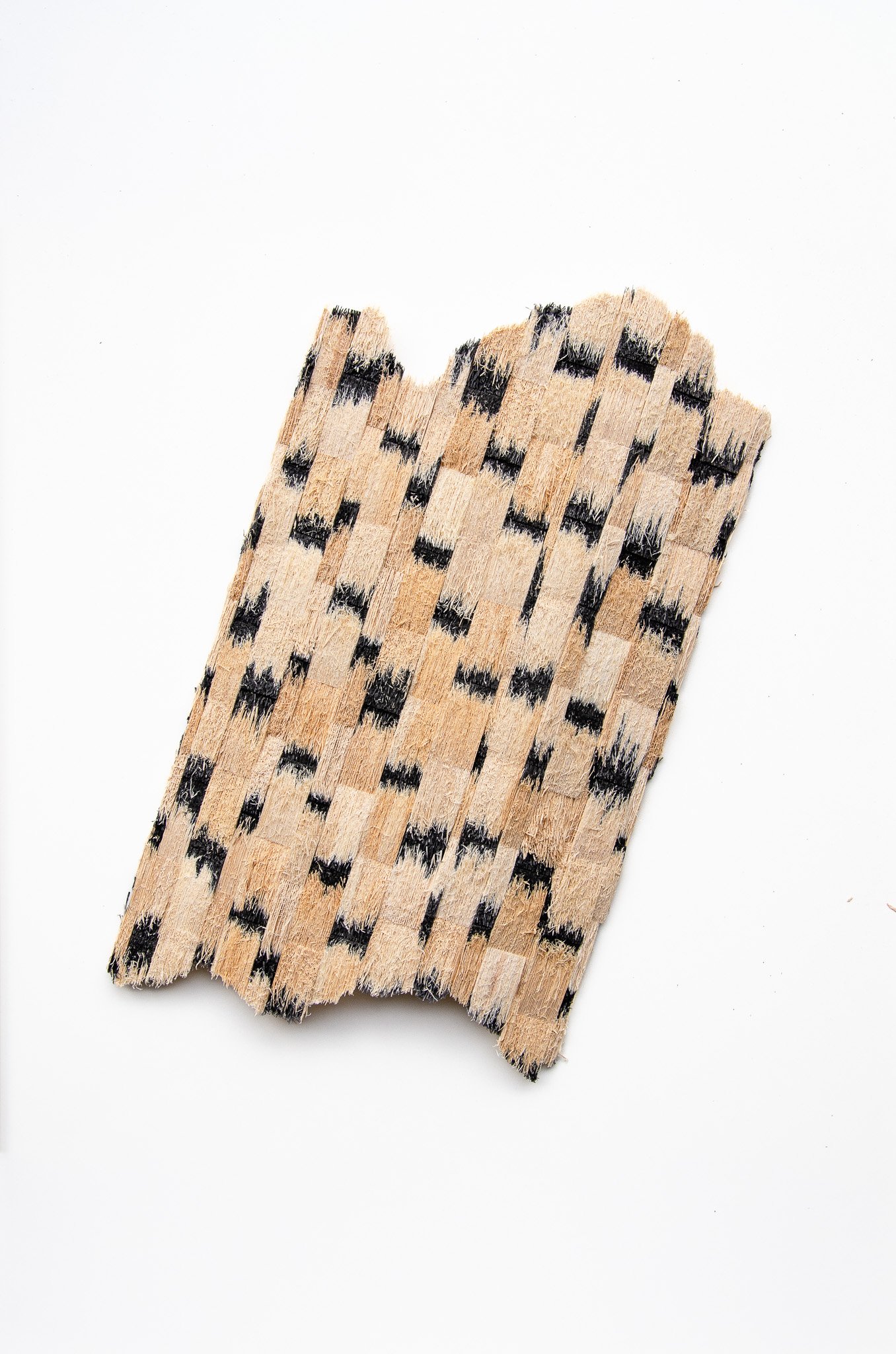 Close-up of a worn wooden object with black checkered pattern markings, placed on a white background.