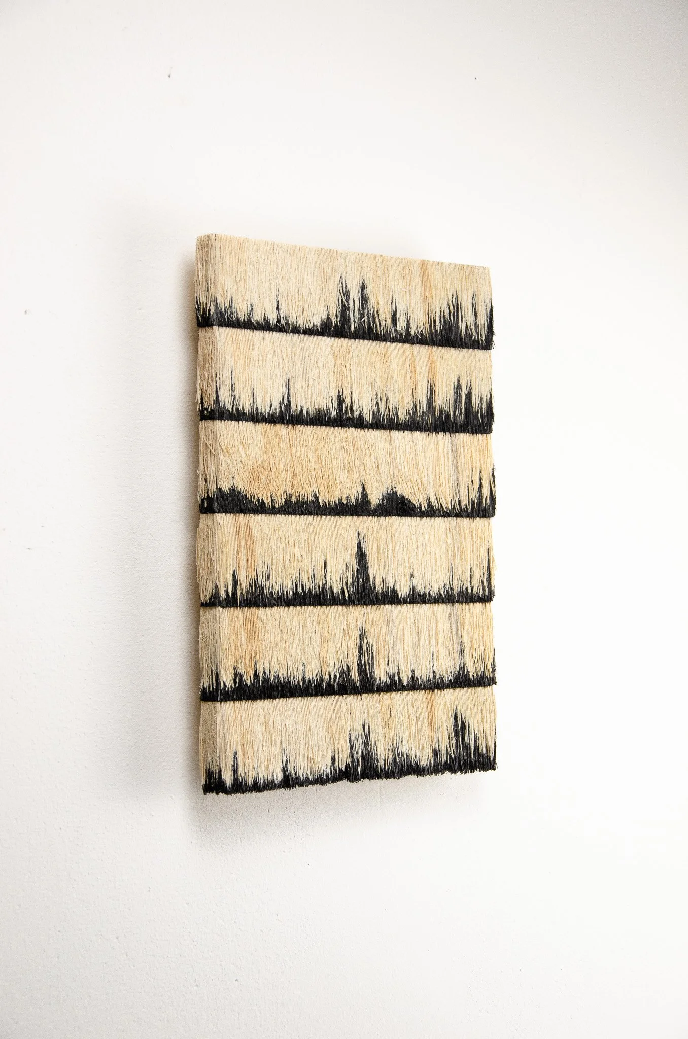 Close-up of a paintbrush with black paint on machine-cut bristles against a white wall.