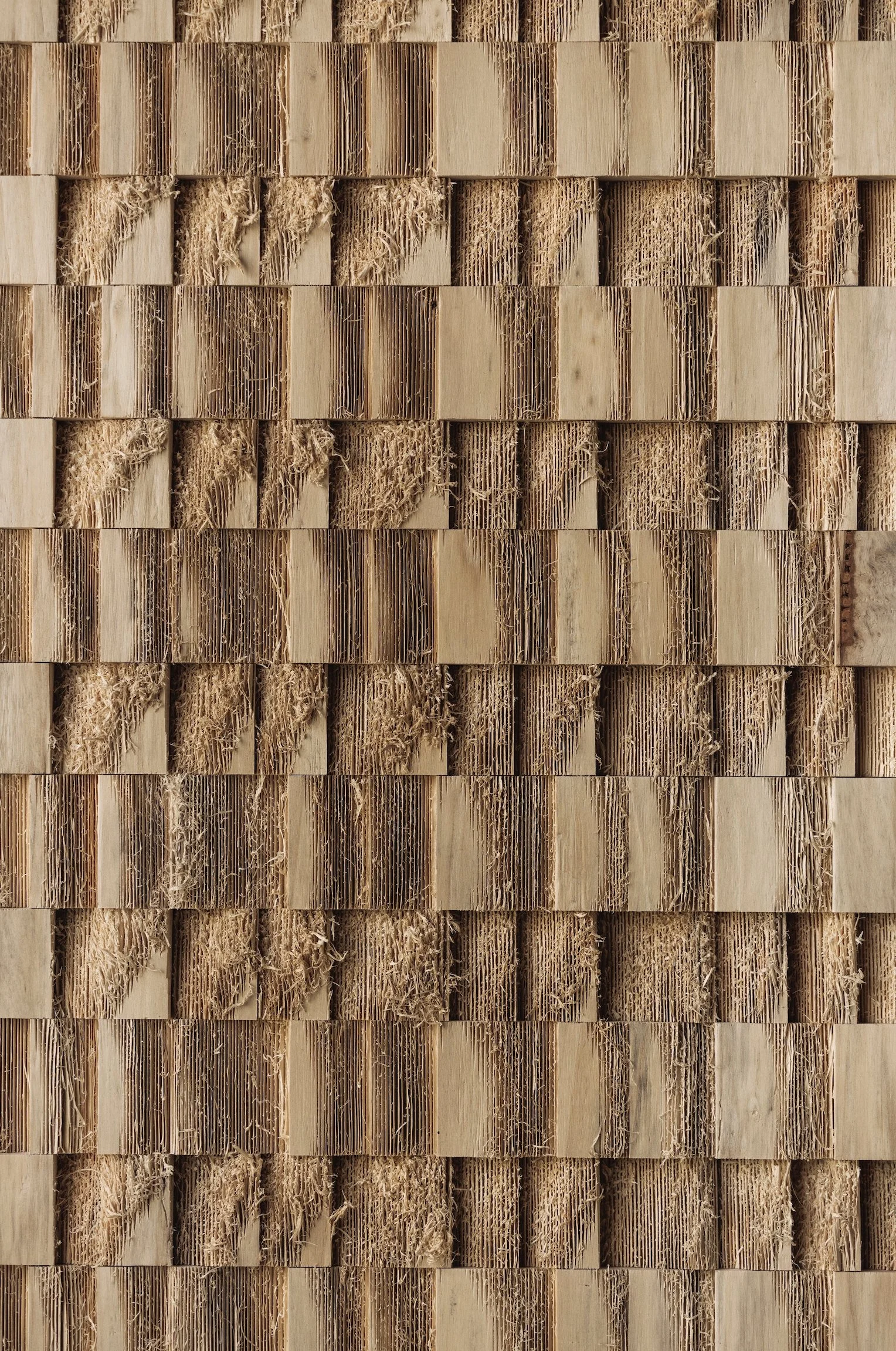 Close-up of a textured surface made of numerous small wooden blocks arranged in horizontal rows, with some blocks showing exposed fibrous interior.