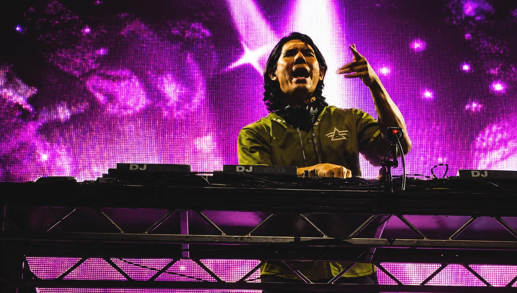 DJ performing on stage with a pink and purple cosmic background display.