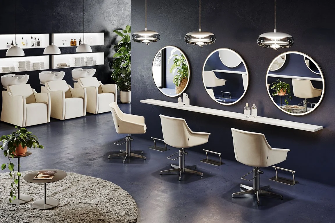 Salon de coiffure moderne avec quatre fauteuils de coiffure en face de miroirs ronds, un mur peint en noir, avec des étagères blanches, des lampes suspendues métalliques, et des plantes décoratives.