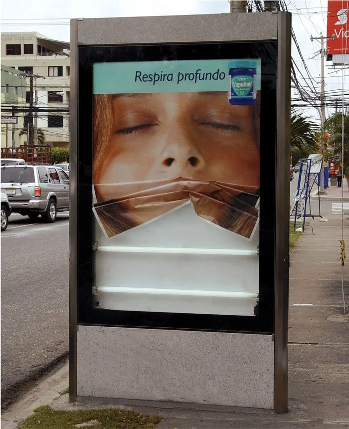 An outdoor advertisement billboard with a large image of a woman with closed eyes and a facial expression suggestive of deep breathing or relaxation. The billboard has a sign that says "Respi real profundo" and a small image of Vicks VapoRub in the t