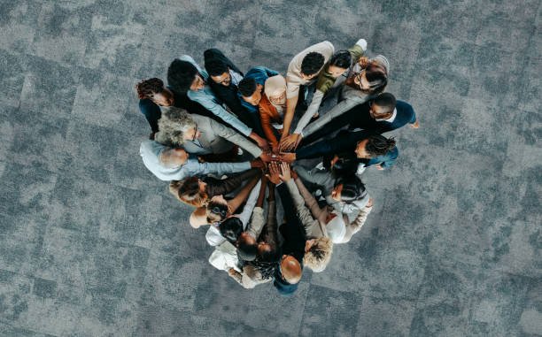 Overhead view of a diverse group of people in business attire gathered in a circle, each extending a hand toward the center.