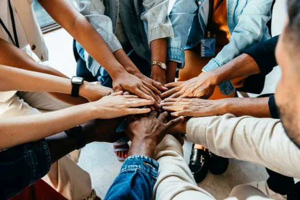 Multiple people putting their hands together in a group hug.