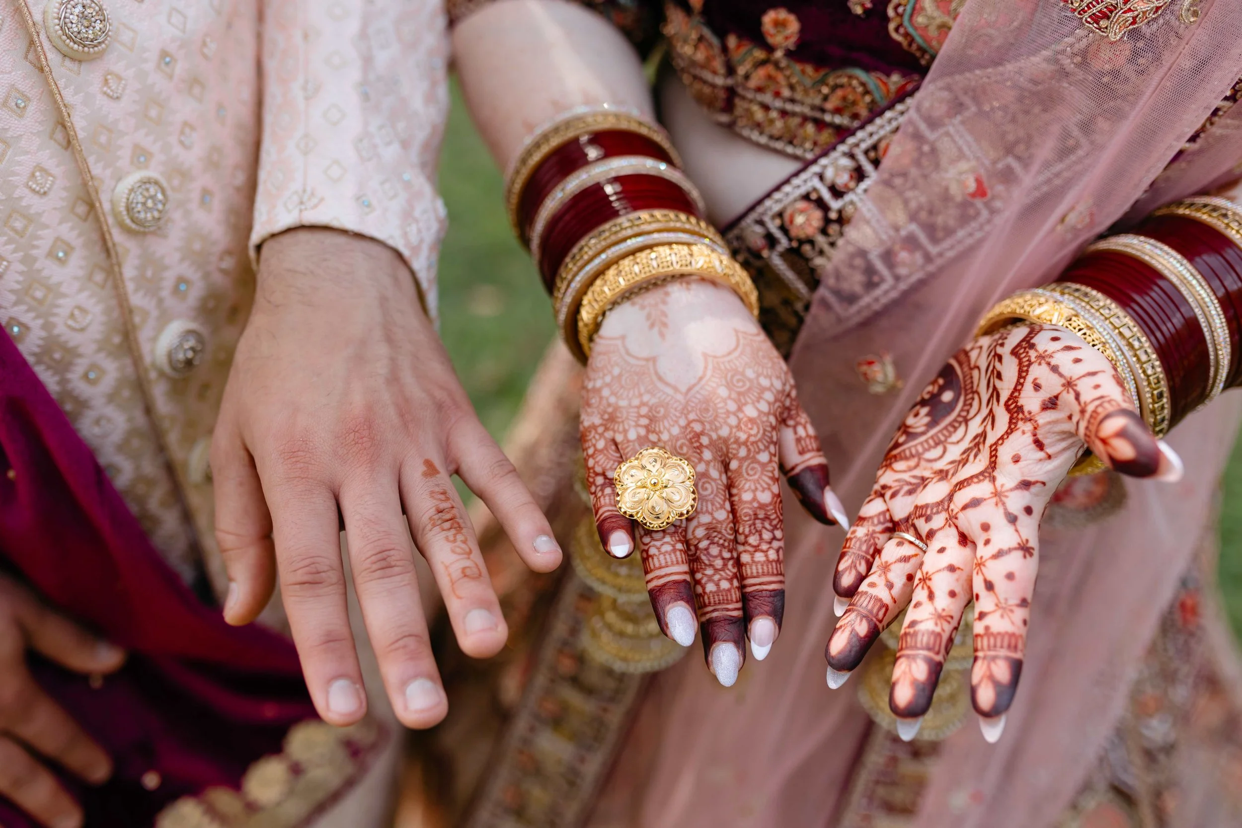 Close-up of hands and arms adorned with traditional jewelry, mehndi (henna) designs, and colorful clothing, indicating a cultural or festive occasion.