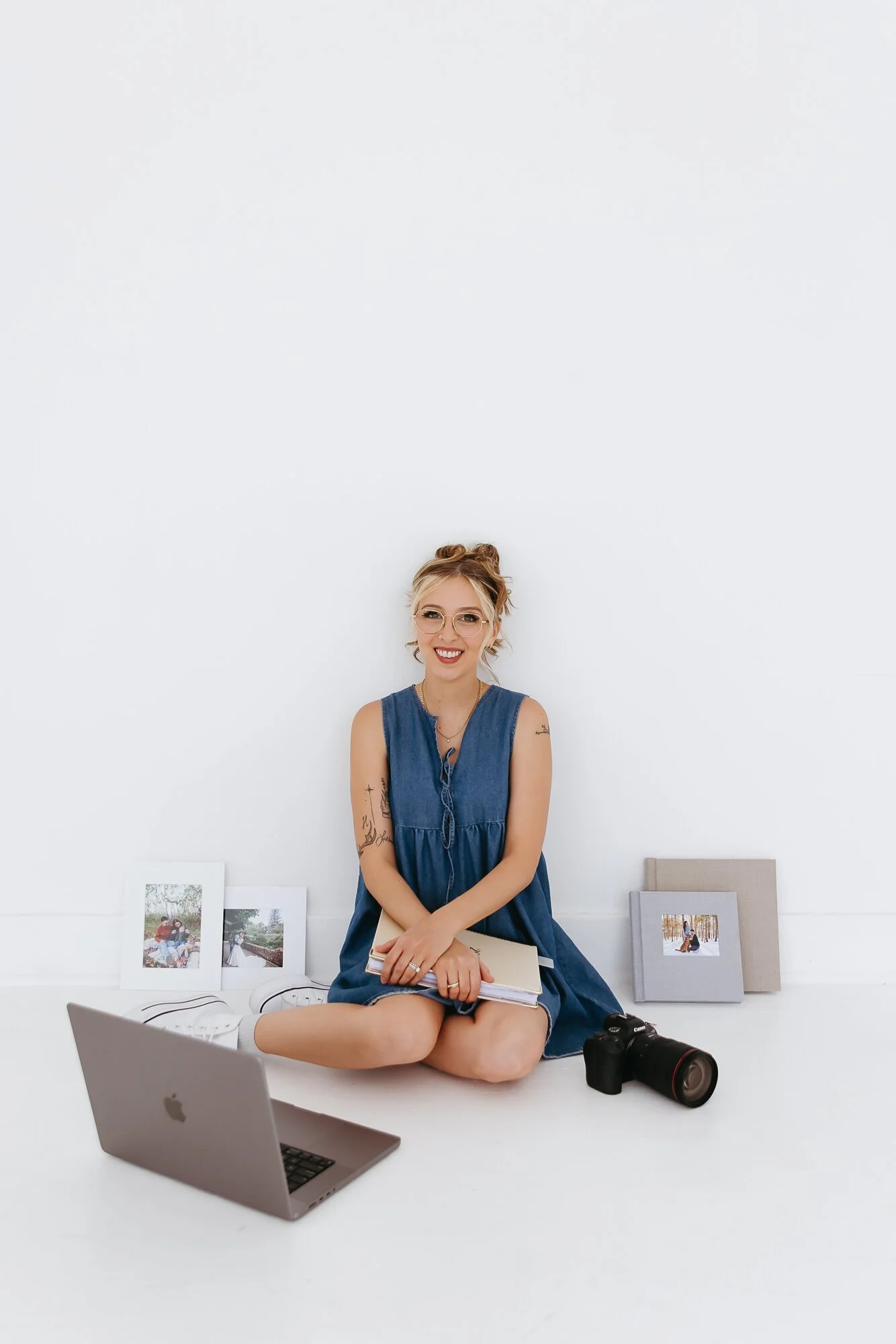 Winnipeg photographer sitting surrounded by photo albums and professional prints with her camera, planner and laptop nearby